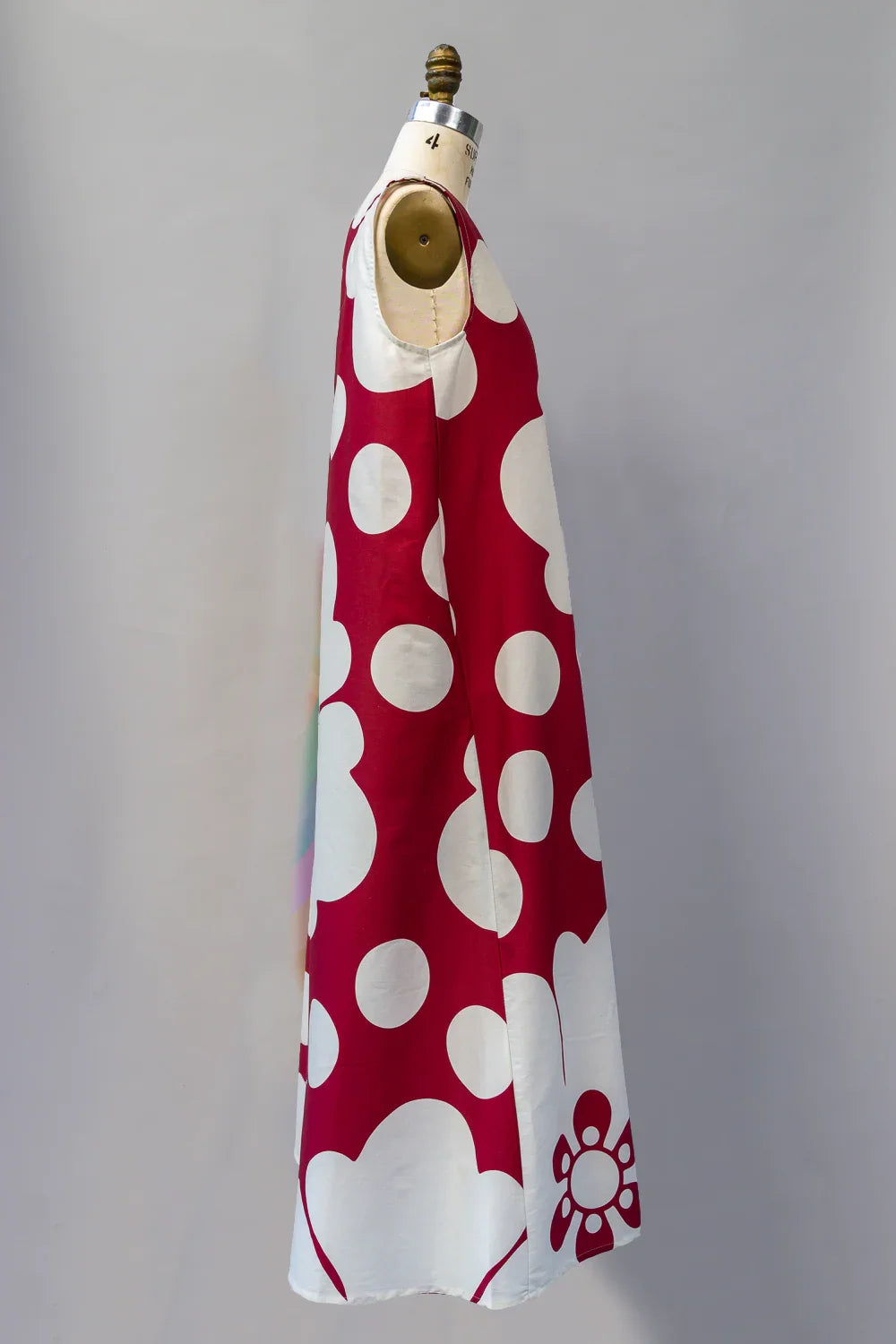 Long red muumuu dress with large white polka dots and floral print, side view on mannequin.