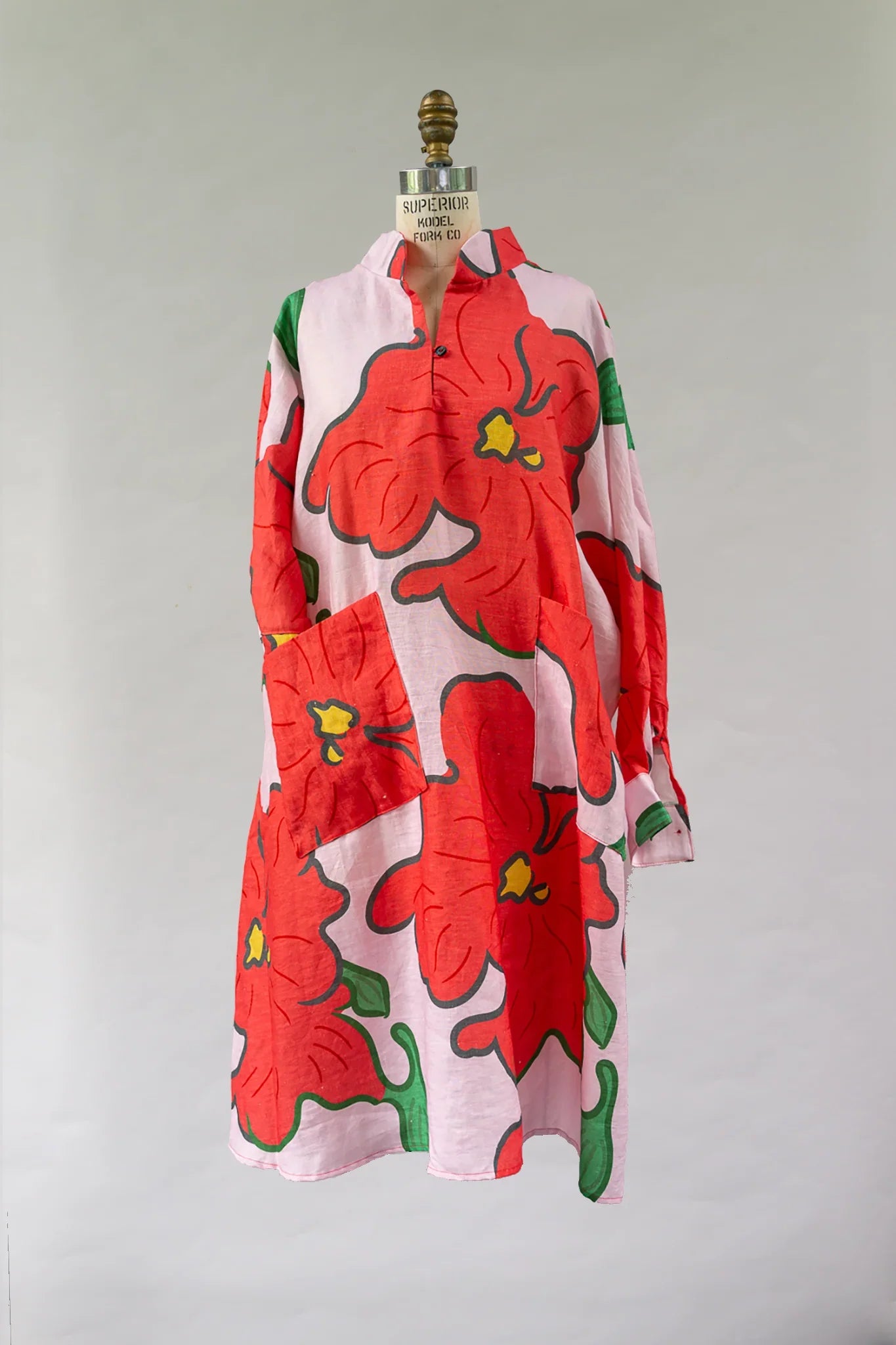 Pink muumuu dress with bold red hibiscus print and green leaves on mannequin