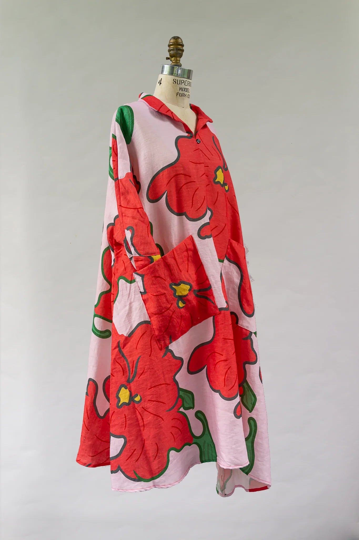 Pink modern muumuu dress with bold red Hawaiian floral print on mannequin