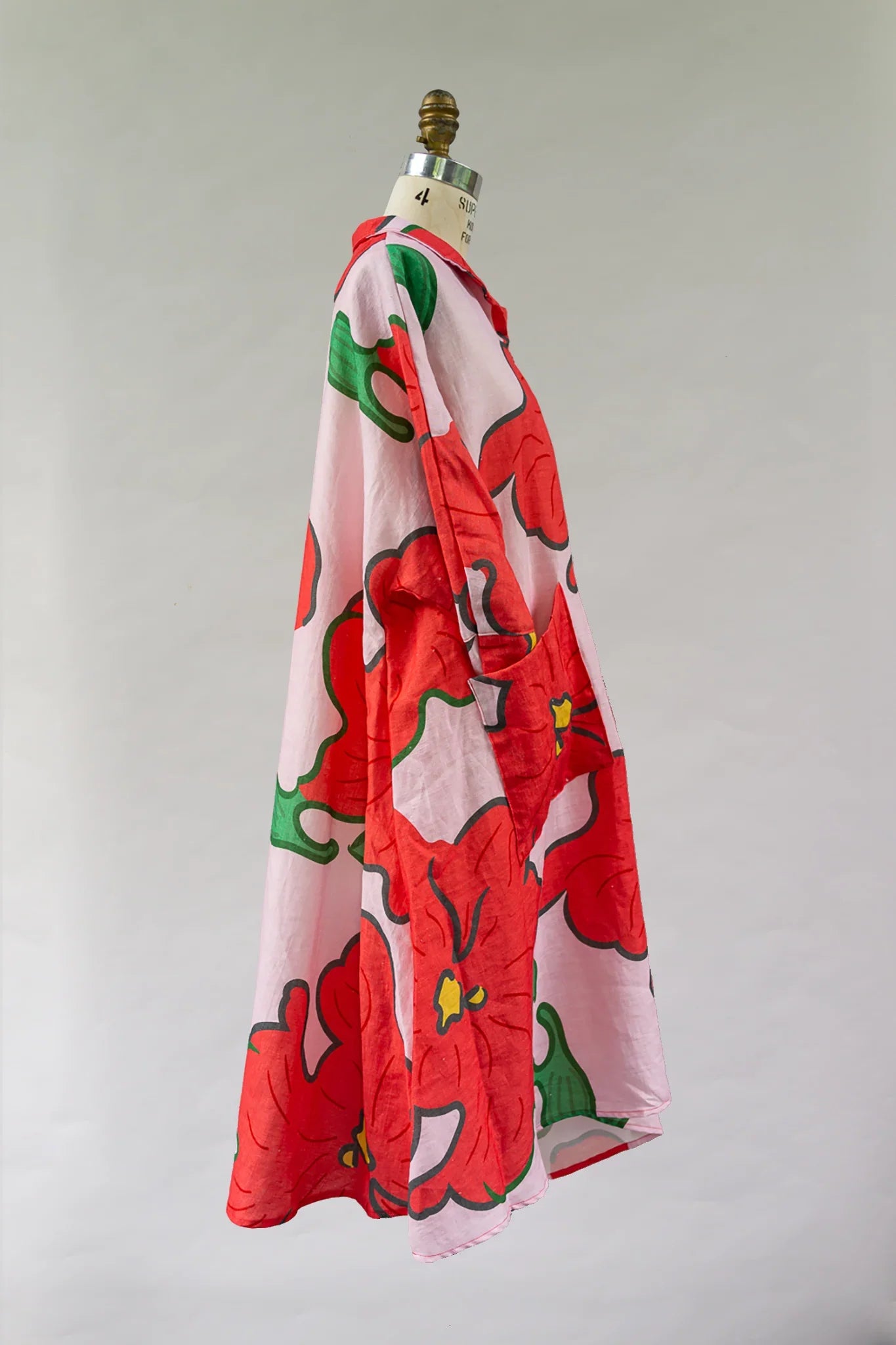 Flowy muumuu dress with bold red floral and green leaf Hawaiian print on pink fabric