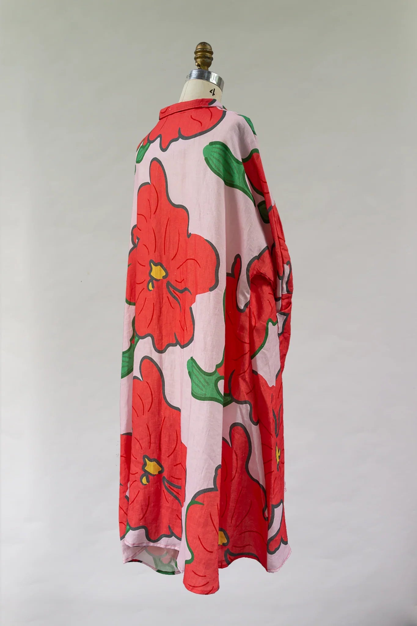 Pink muumuu dress with bold red hibiscus print and green leaves on a mannequin