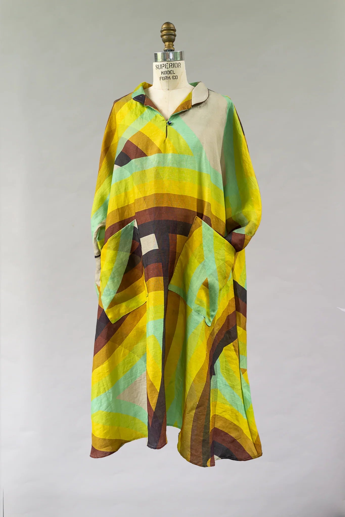 Colorful mu'umu'u dress with yellow, green, and brown abstract Hawaiian print on mannequin