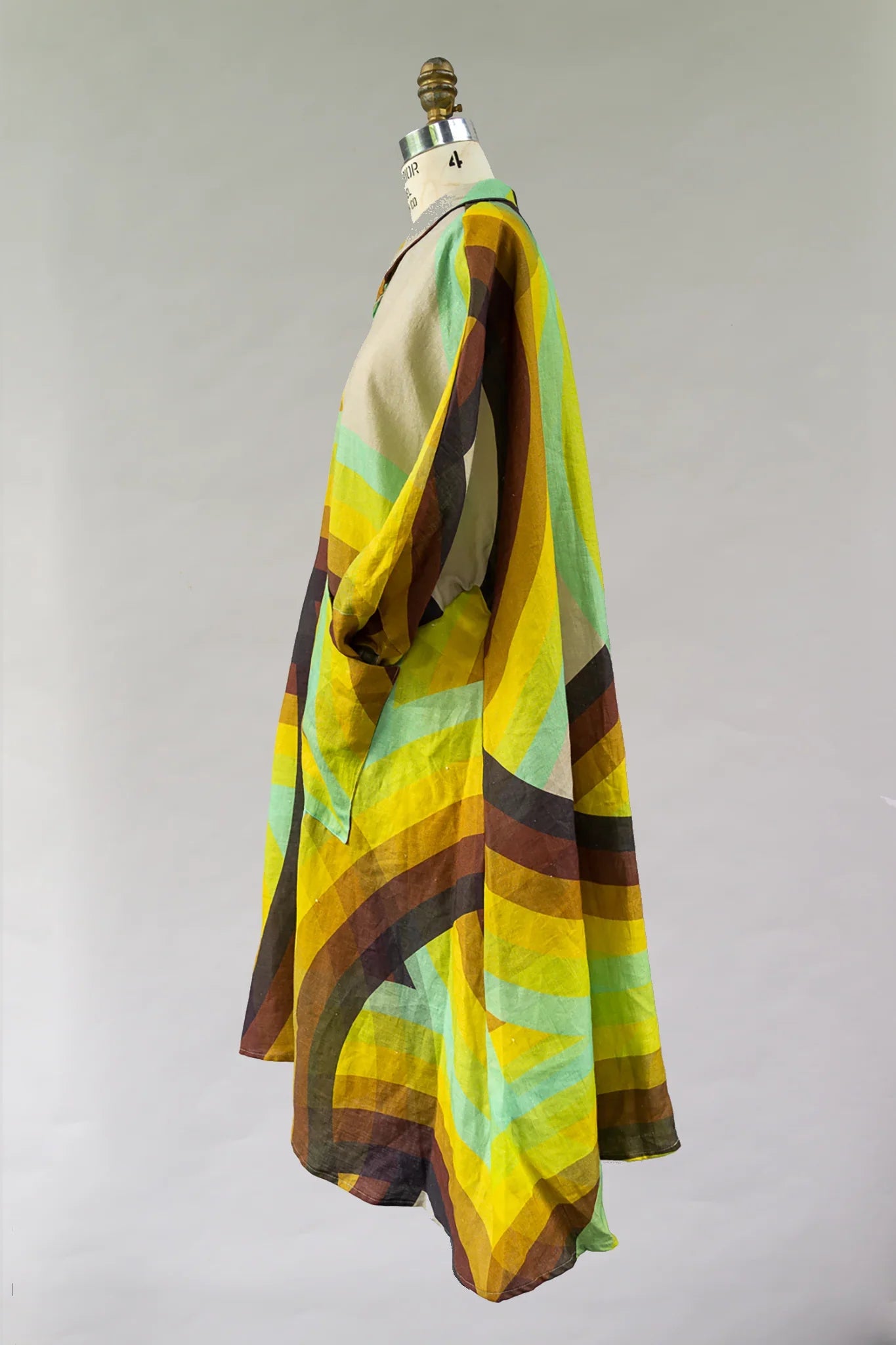 Modern muumuu dress with bold yellow, green, and brown geometric Hawaiian print on mannequin