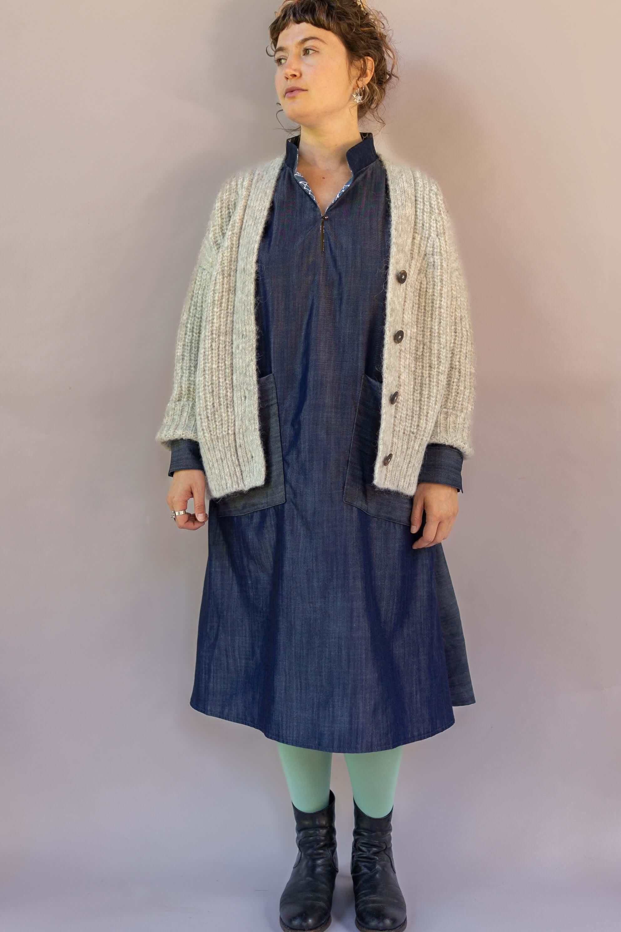 Woman wearing denim muumuu dress, chunky knit cardigan, mint tights, and black boots
