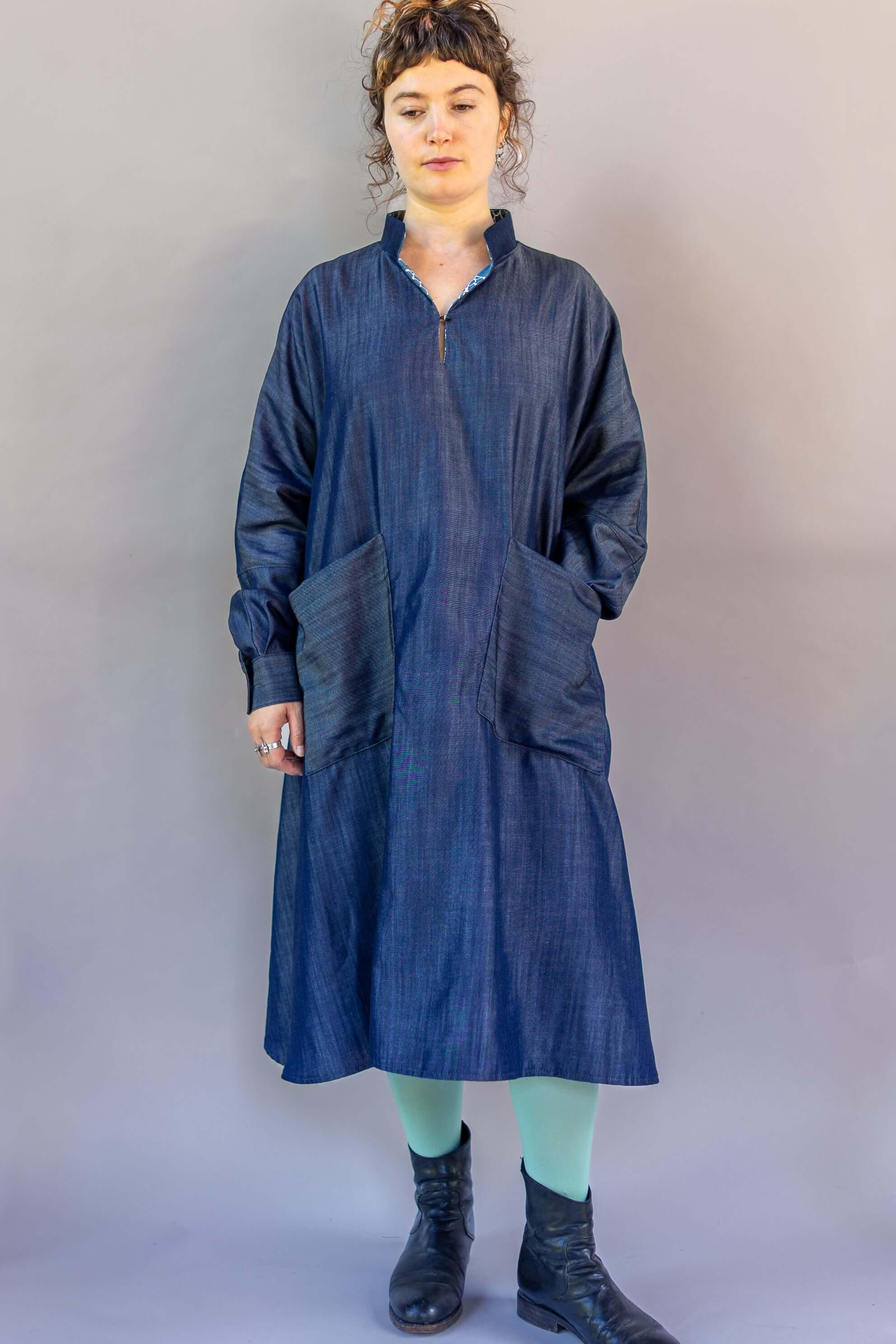 Woman wearing a loose-fit denim muumuu dress with large front pockets and black ankle boots