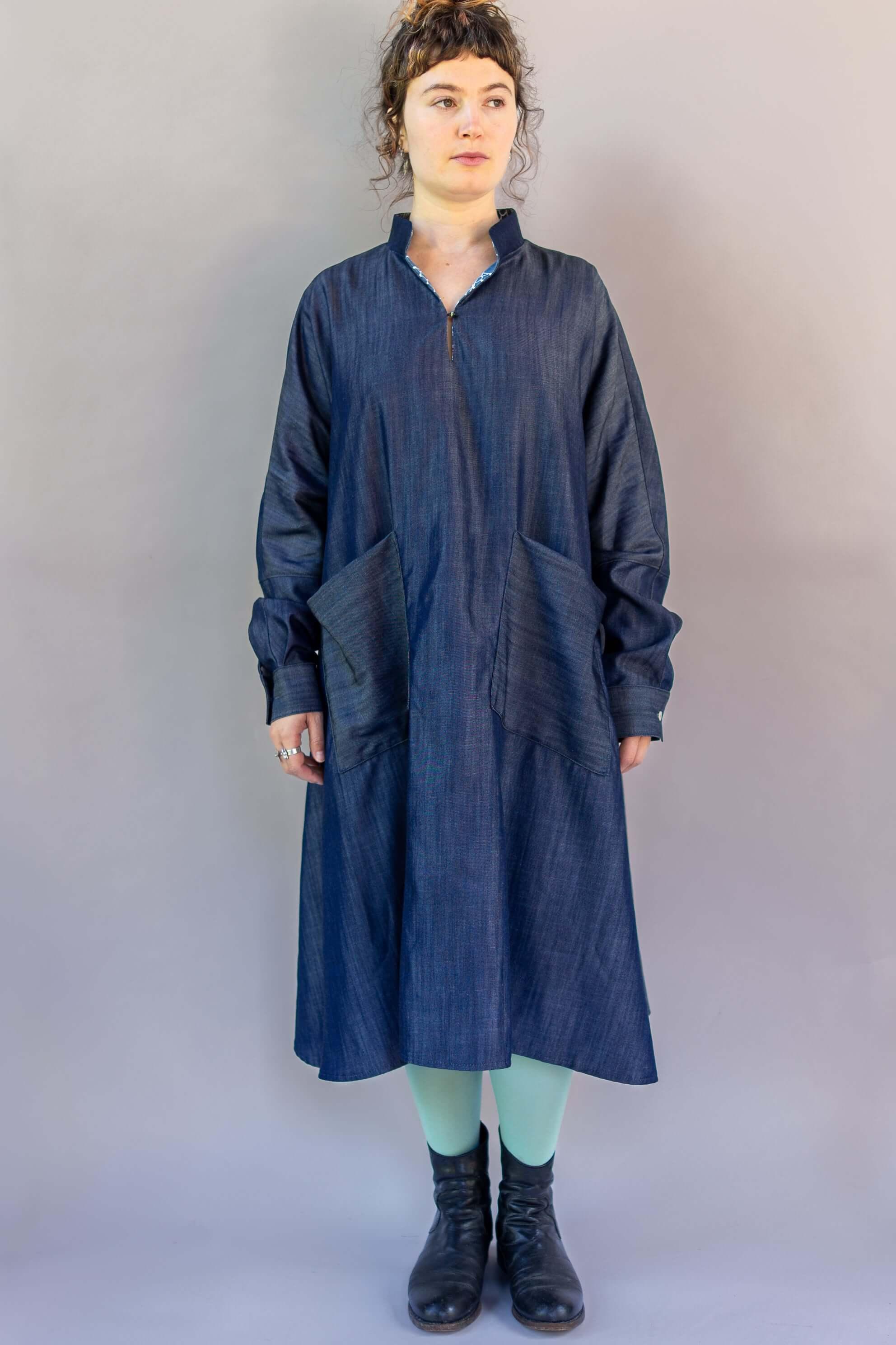 Woman wearing a long-sleeve denim muumuu dress with large front pockets, boots, and mint tights