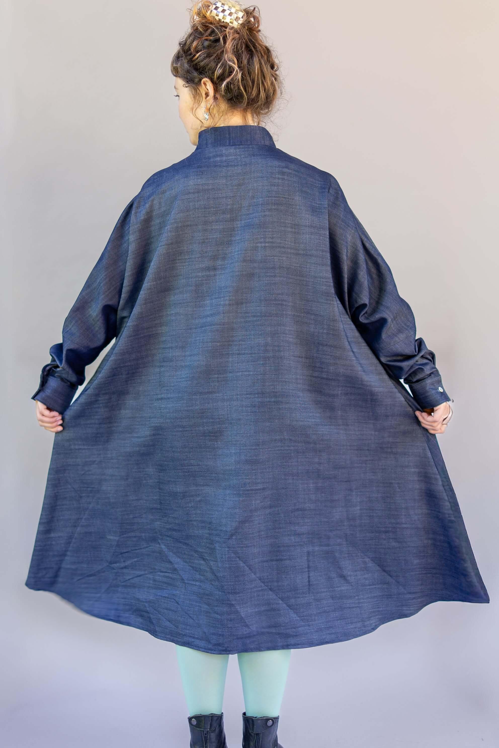 Woman in loose-fitting denim muumuu dress with long sleeves, seen from the back