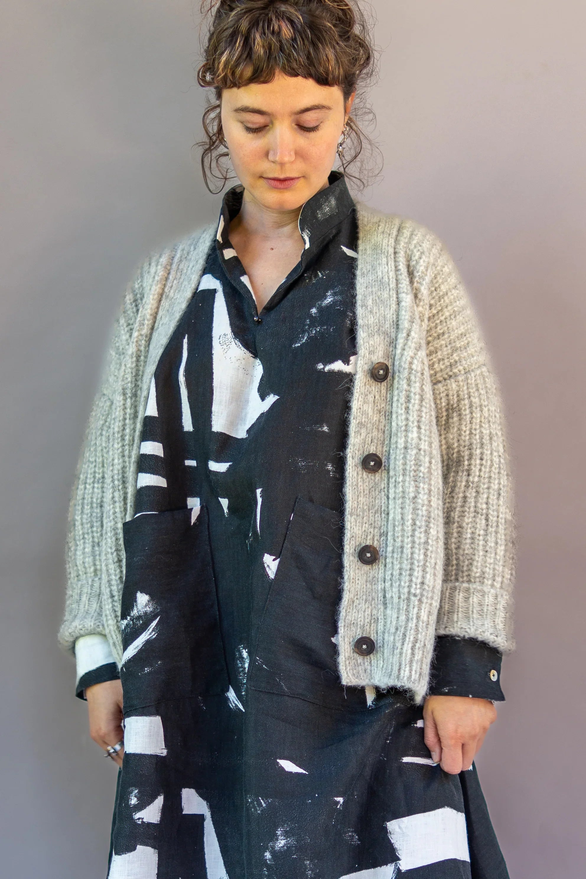 Woman wearing a black and white abstract print mu'umu'u dress with a chunky knit cardigan