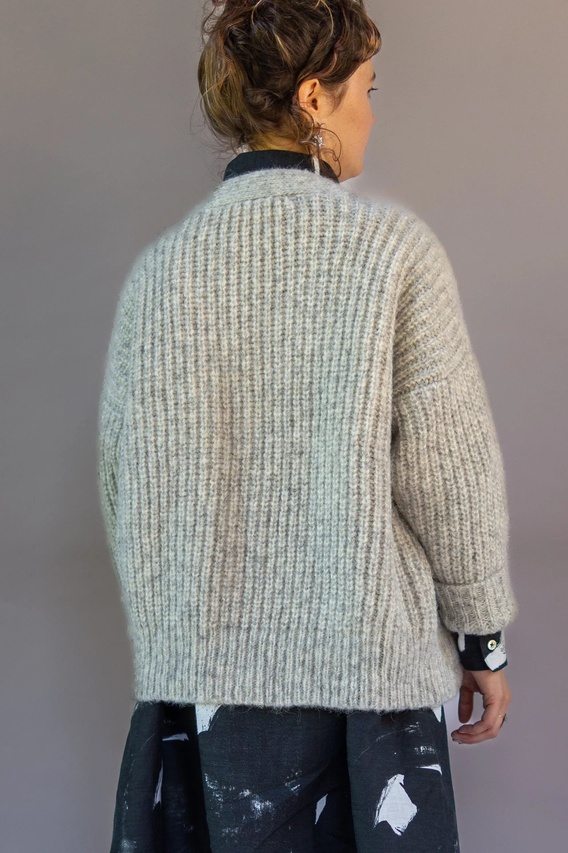 Woman in a chunky knit gray cardigan and black printed dress, shown from the back