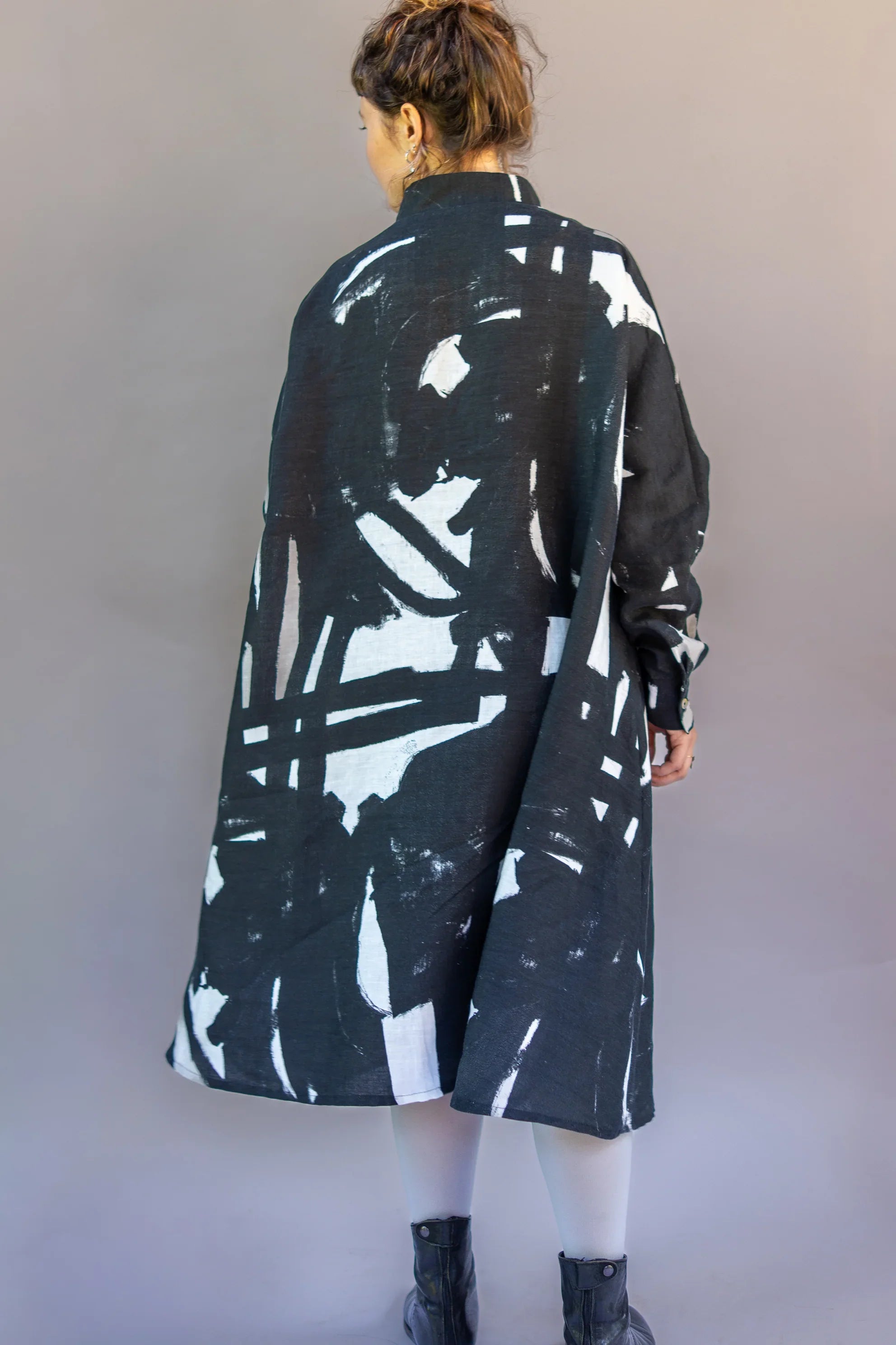 Woman wearing a modern black muumuu dress with abstract white print, standing against a neutral background