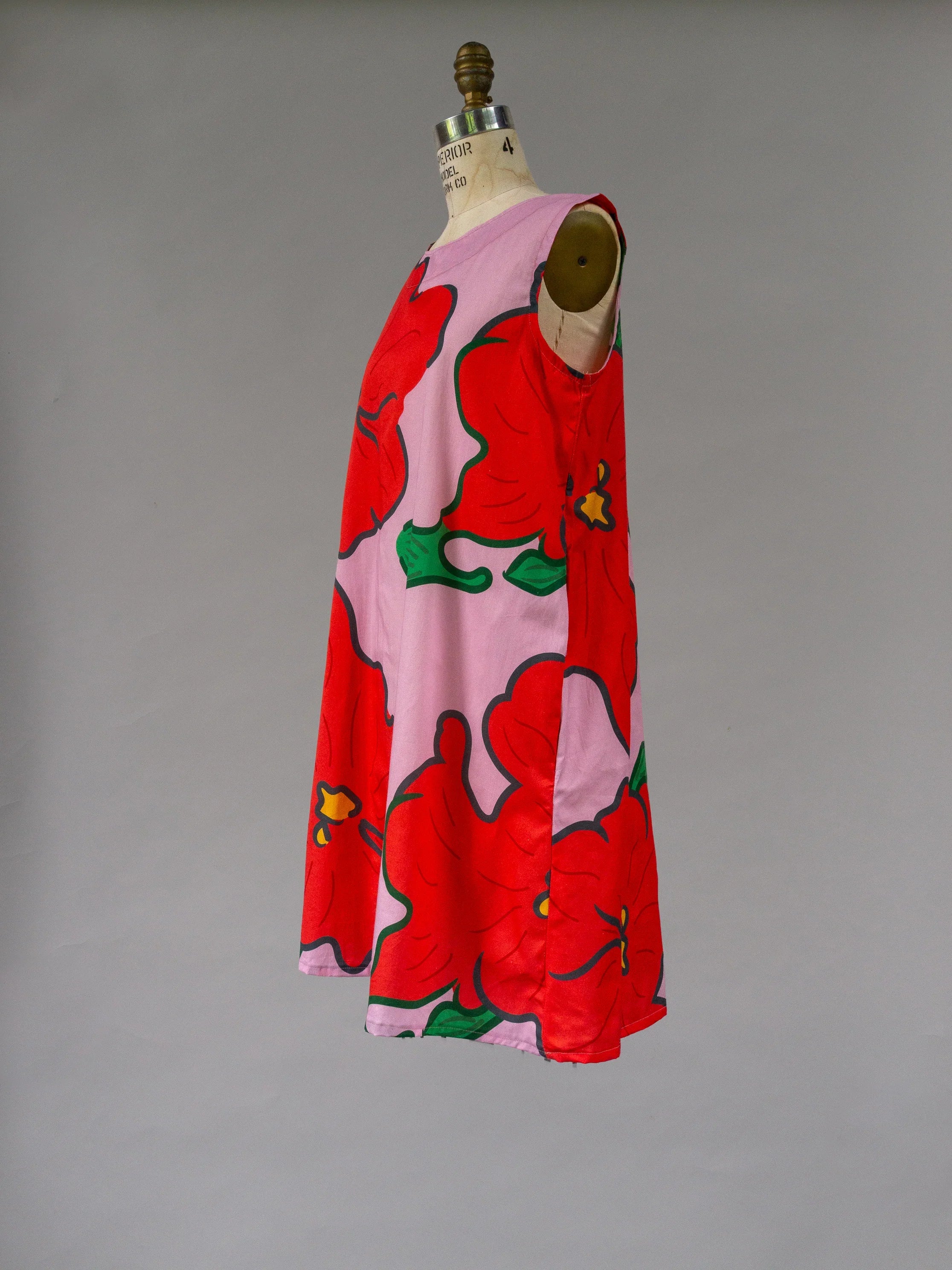 Pink sleeveless muumuu dress with bold red Hawaiian floral print on mannequin