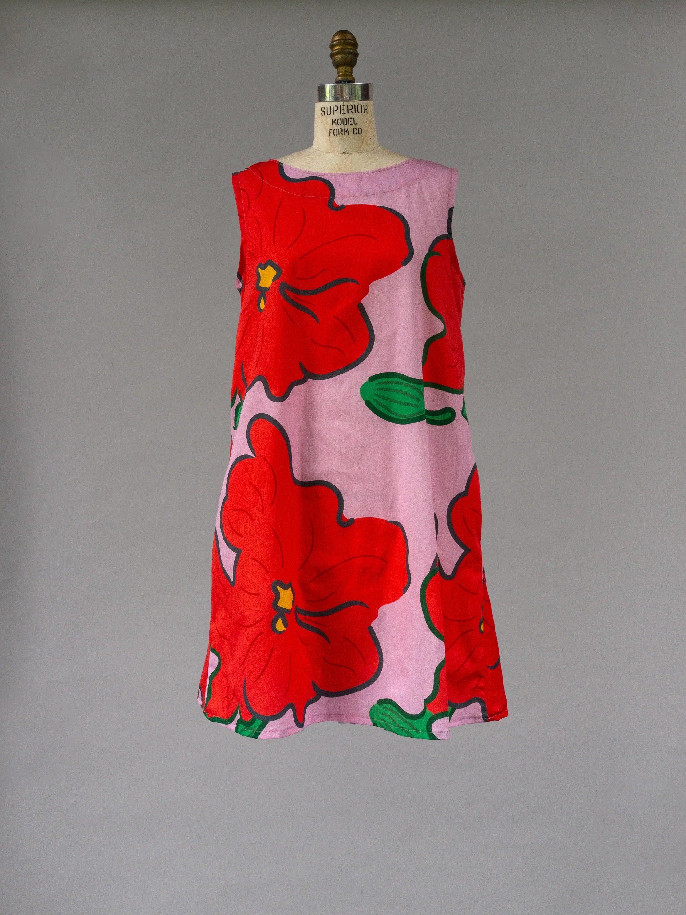 Sleeveless pink muumuu dress with bold red hibiscus Hawaiian print, displayed on mannequin