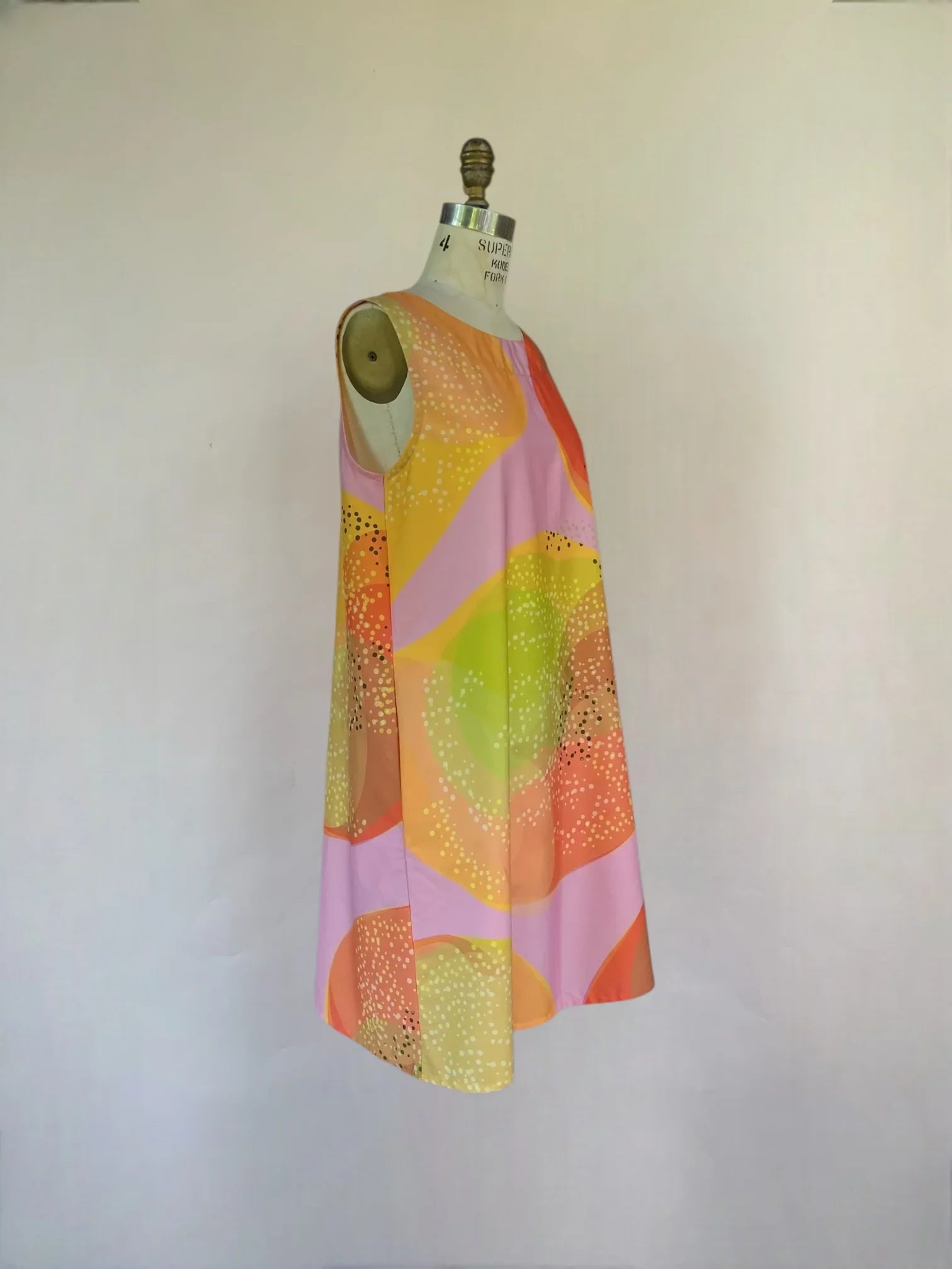 Sleeveless modern muumuu dress with abstract pastel Hawaiian print on mannequin