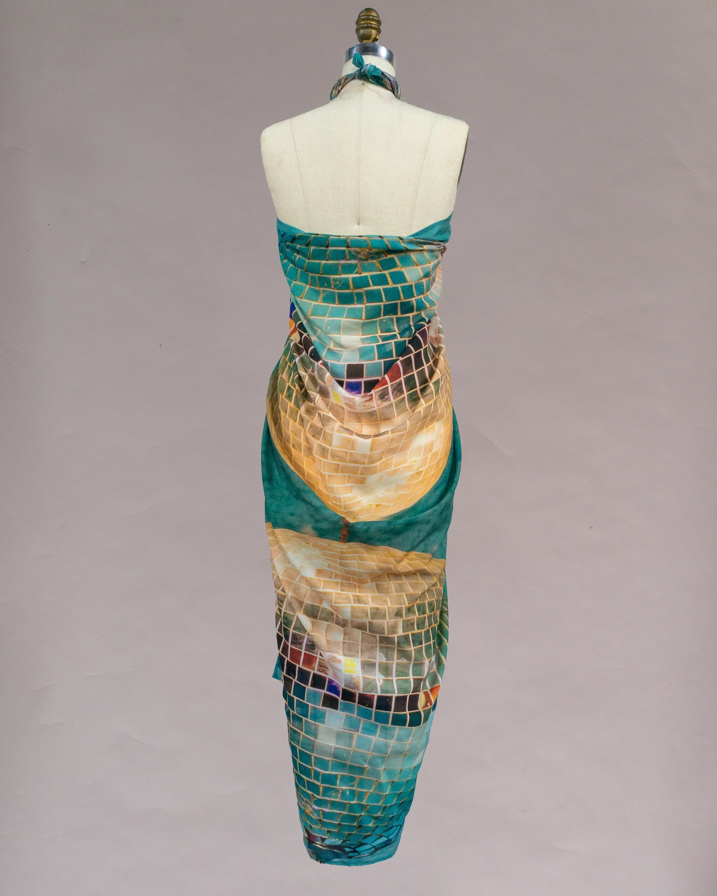 Back view of mannequin wearing pareo with mosaic tile print in teal, gold, and earth tones