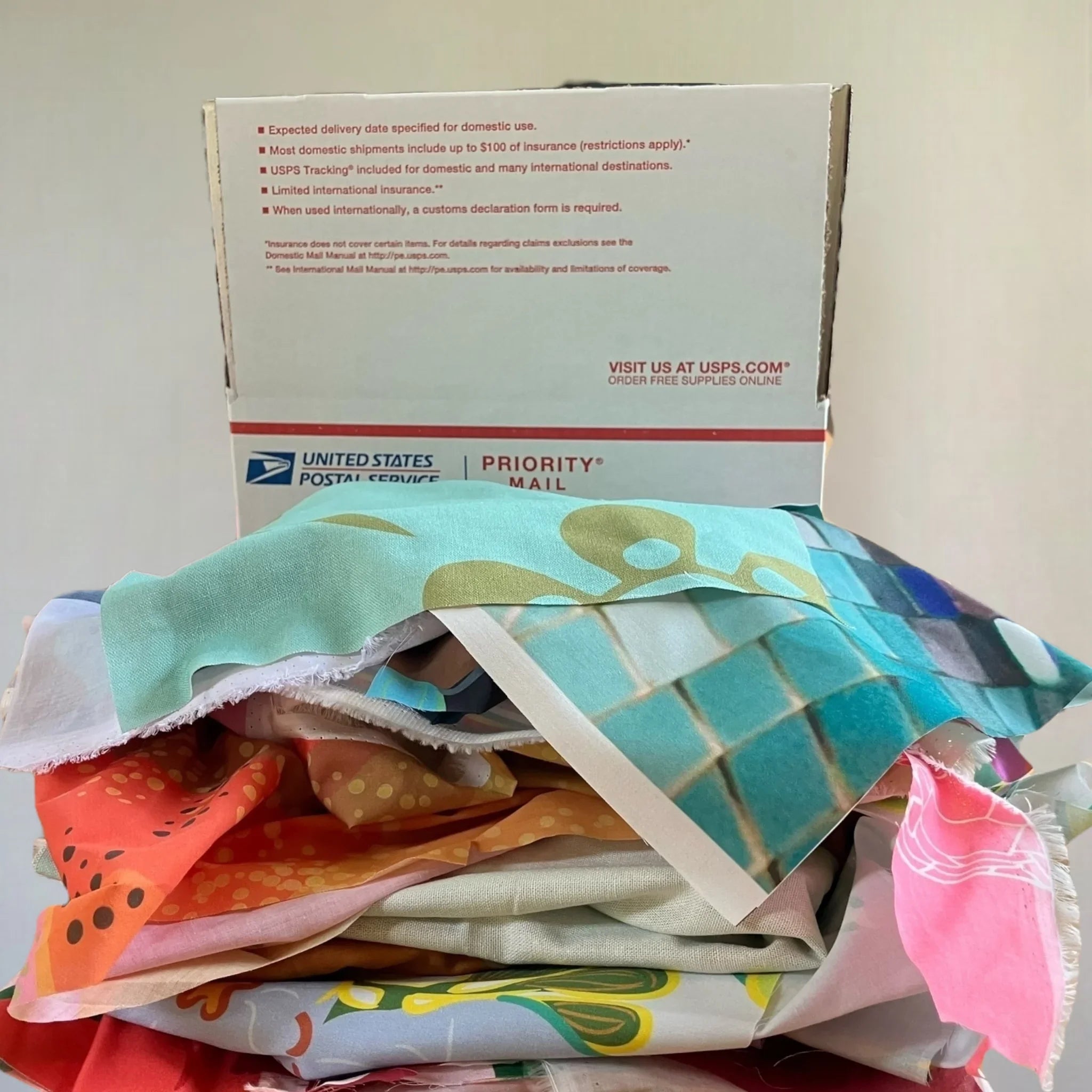 Stack of colorful Hawaiian print fabric in front of USPS Priority Mail box