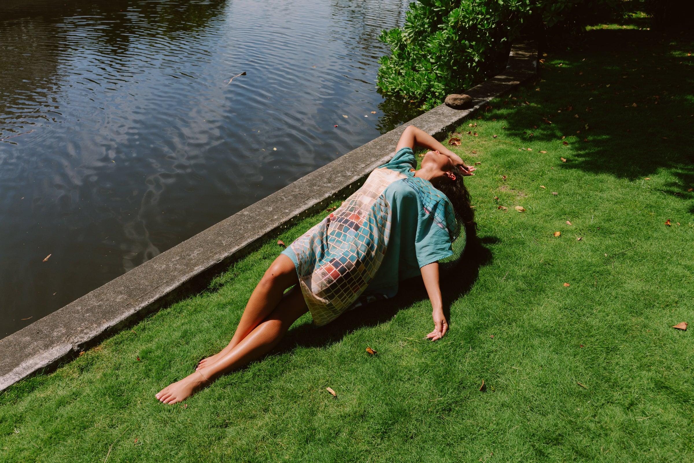 Woman in a modern mu'umu'u dress with Hawaiian print relaxing on grass by water