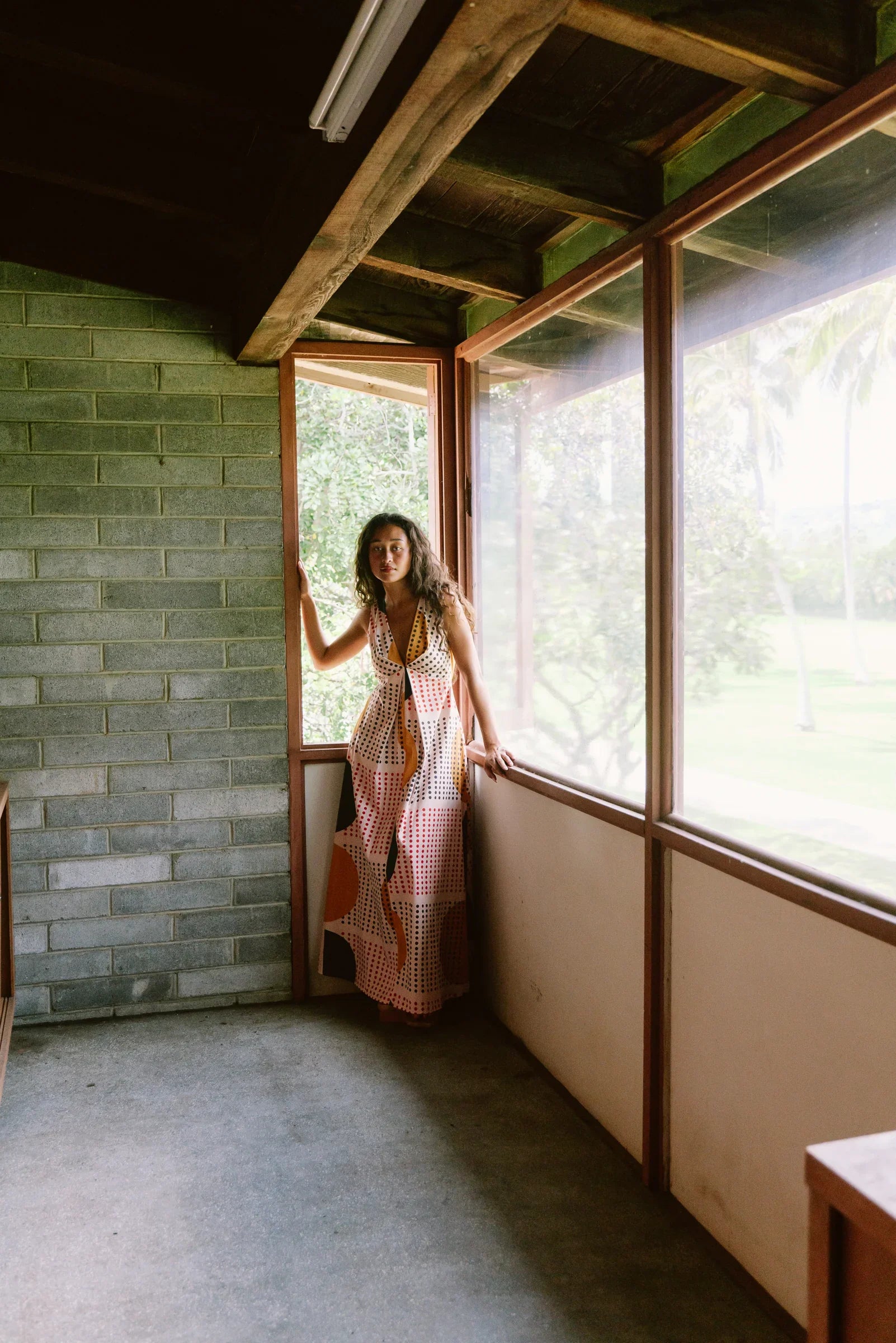 Woman in a modern Hawaiian mu'umu'u dress with geometric prints standing by large windows