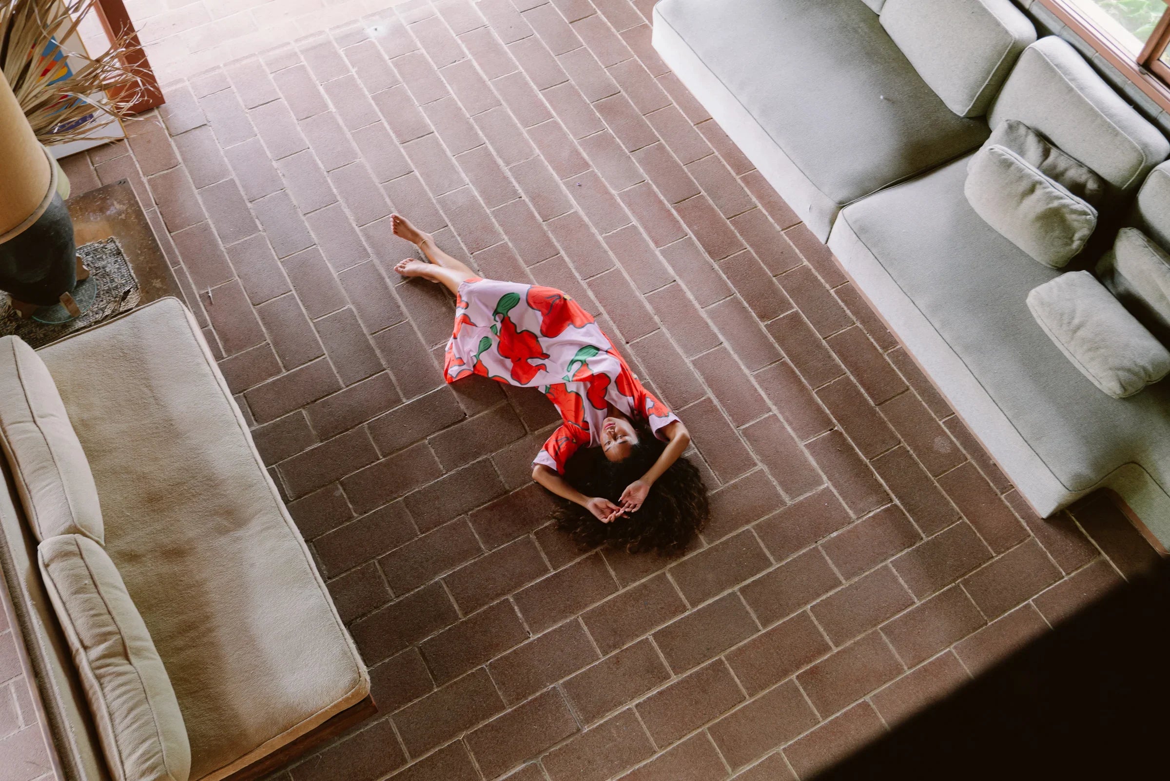 Woman in a colorful floral mu'umu'u dress lying on a brick floor between modern sofas