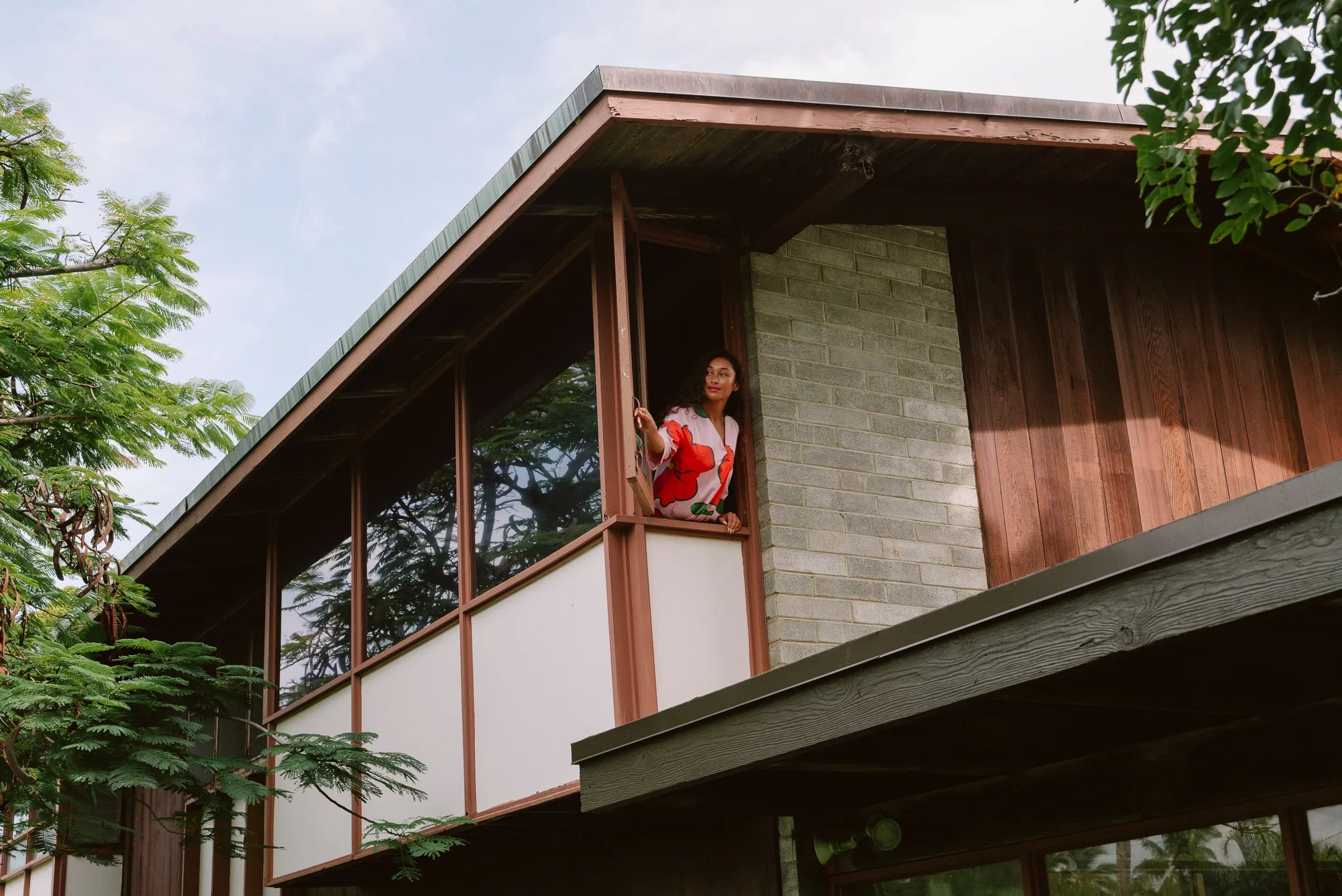 Woman in a colorful modern muumuu dress standing on a balcony of a mid-century house
