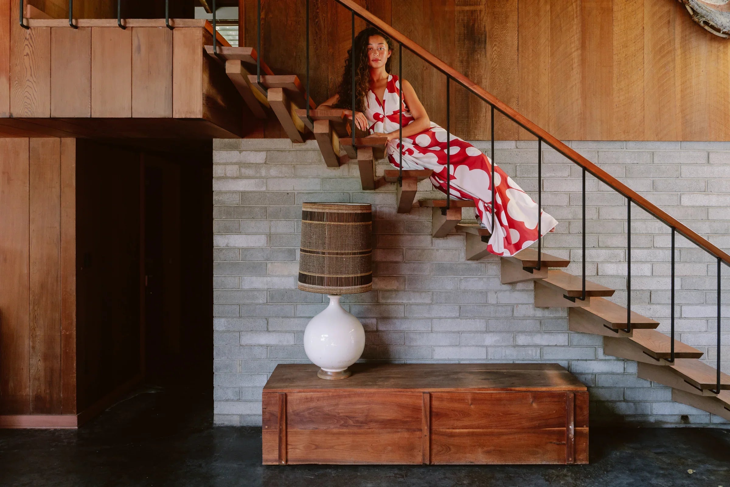 Woman in a modern muumuu dress with large red and white floral print on stairs, mid-century interior