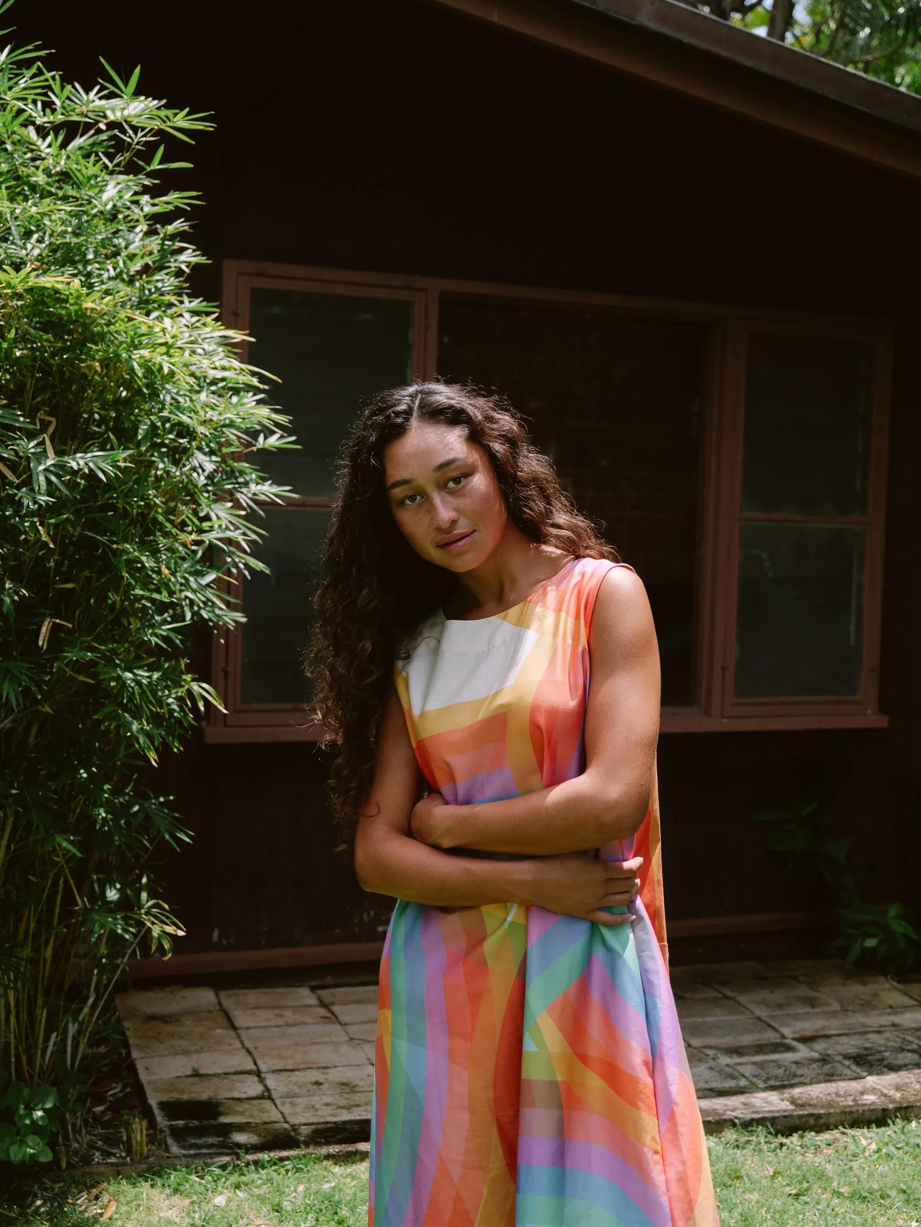 Woman in modern mu'umu'u dress with colorful geometric print standing outdoors by house