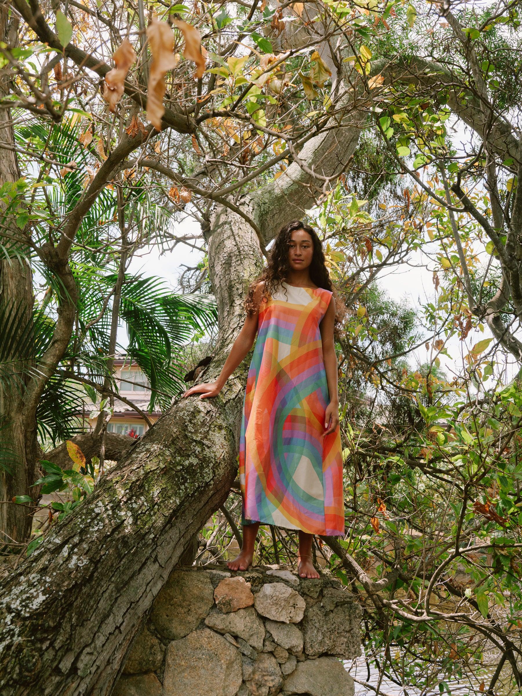 Woman in a colorful modern mu'umu'u dress standing outdoors among tropical trees