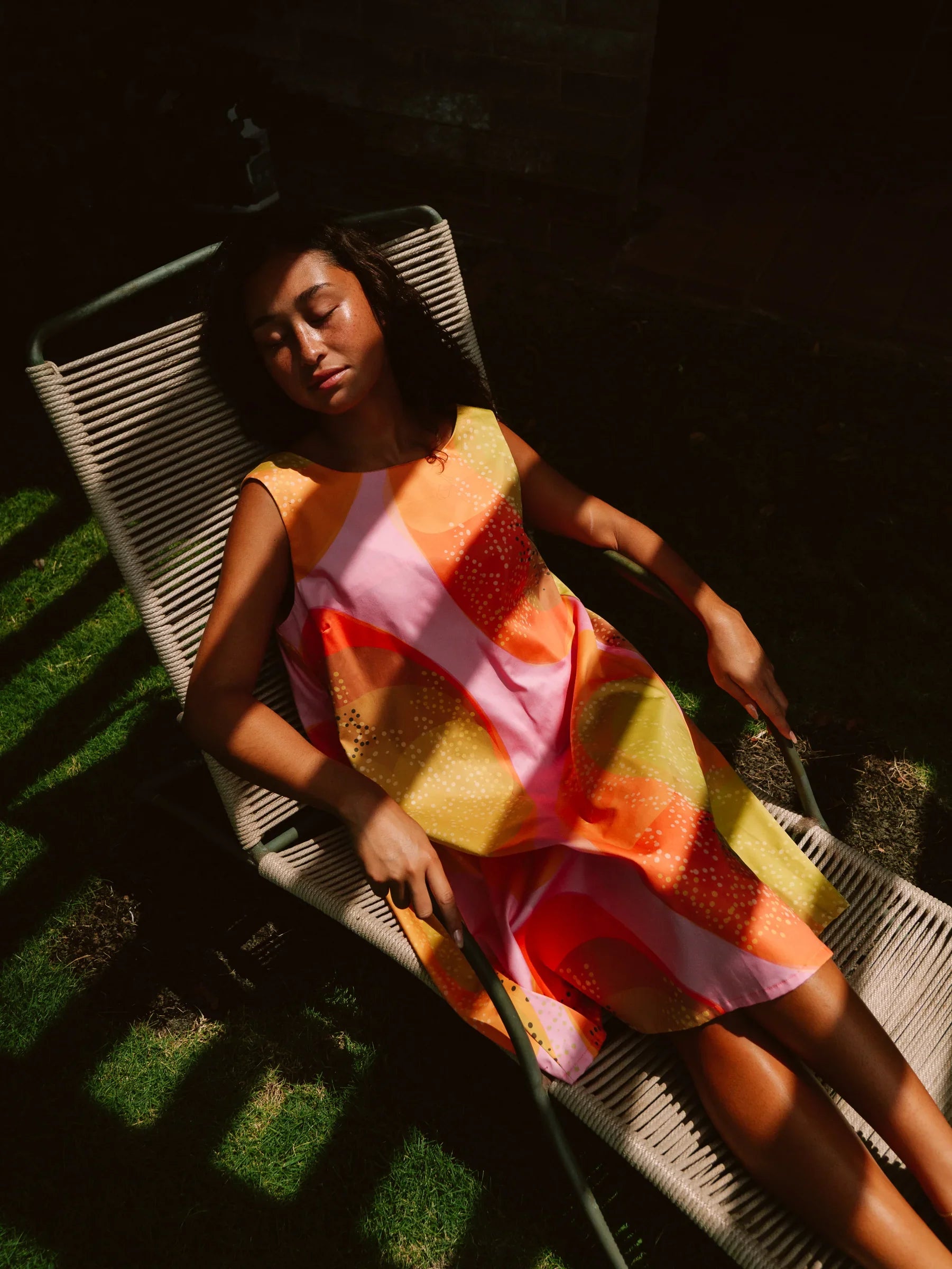 Woman relaxing outdoors in a colorful modern muumuu dress with Hawaiian print.