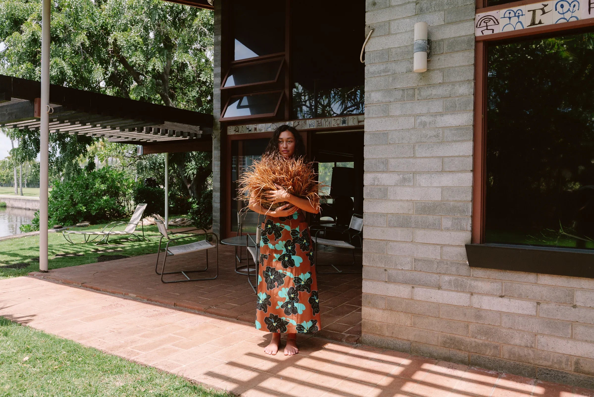 Woman in modern mu'umu'u dress with bold Hawaiian floral print standing on patio