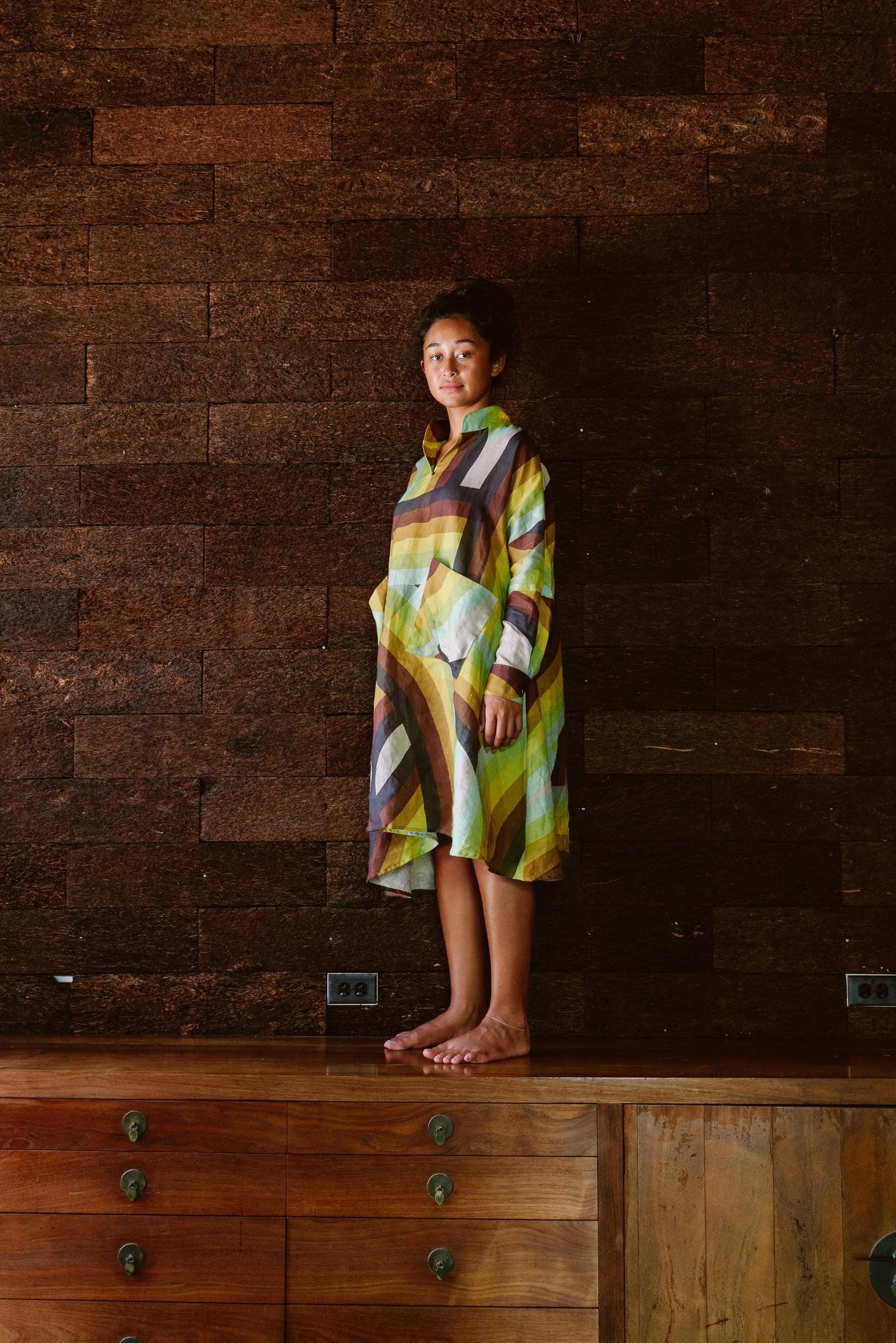 Woman in a modern Hawaiian print mu'umu'u dress with green and brown stripes, standing indoors.