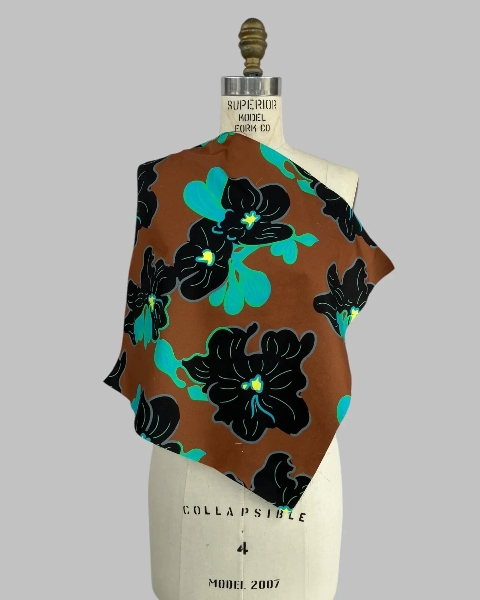 Chestnut brown fabric swatch with bold black and teal Hawaiian floral print on dress form