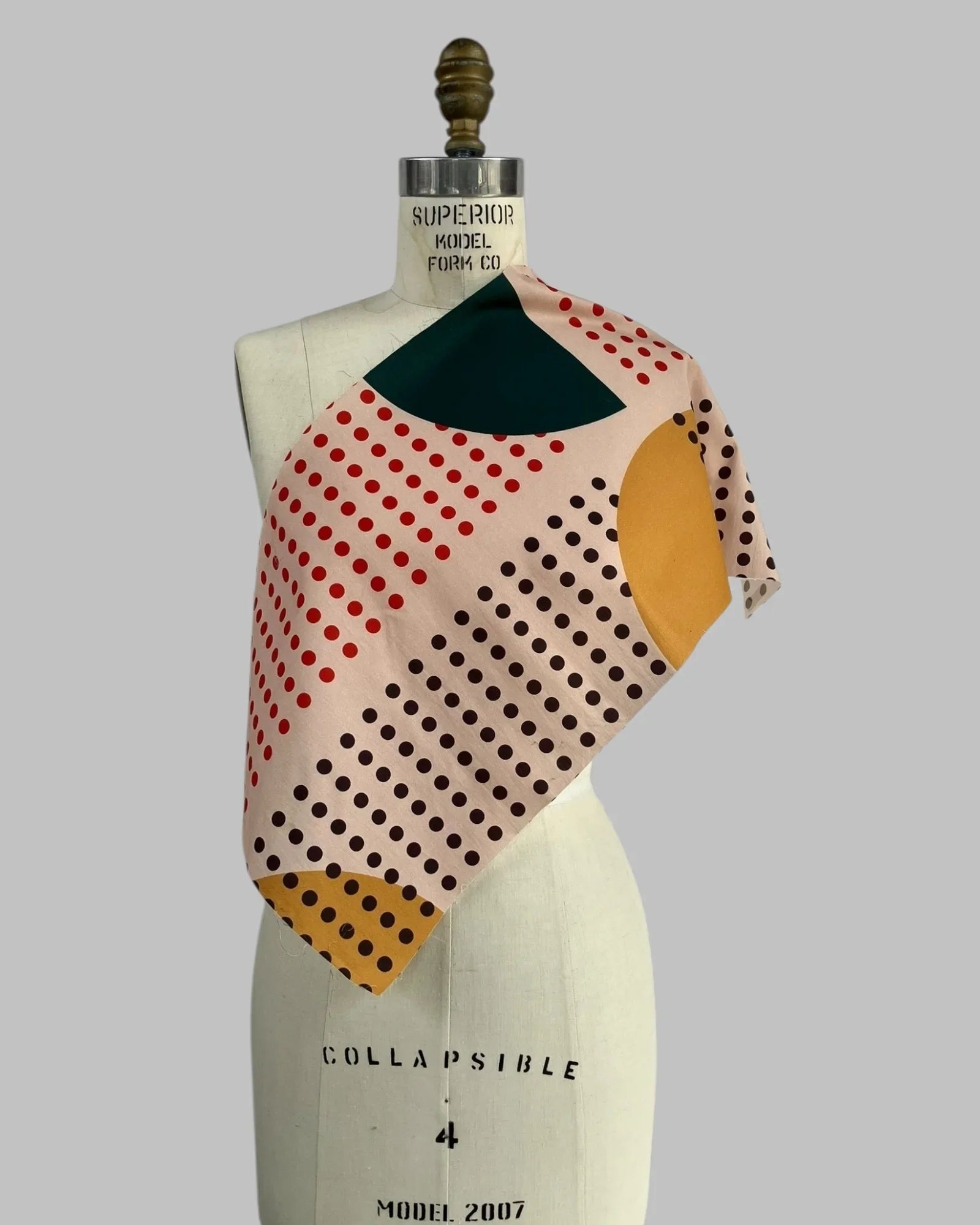 Fabric swatch on mannequin with geometric sunrise print in red, mustard, green, and black dots