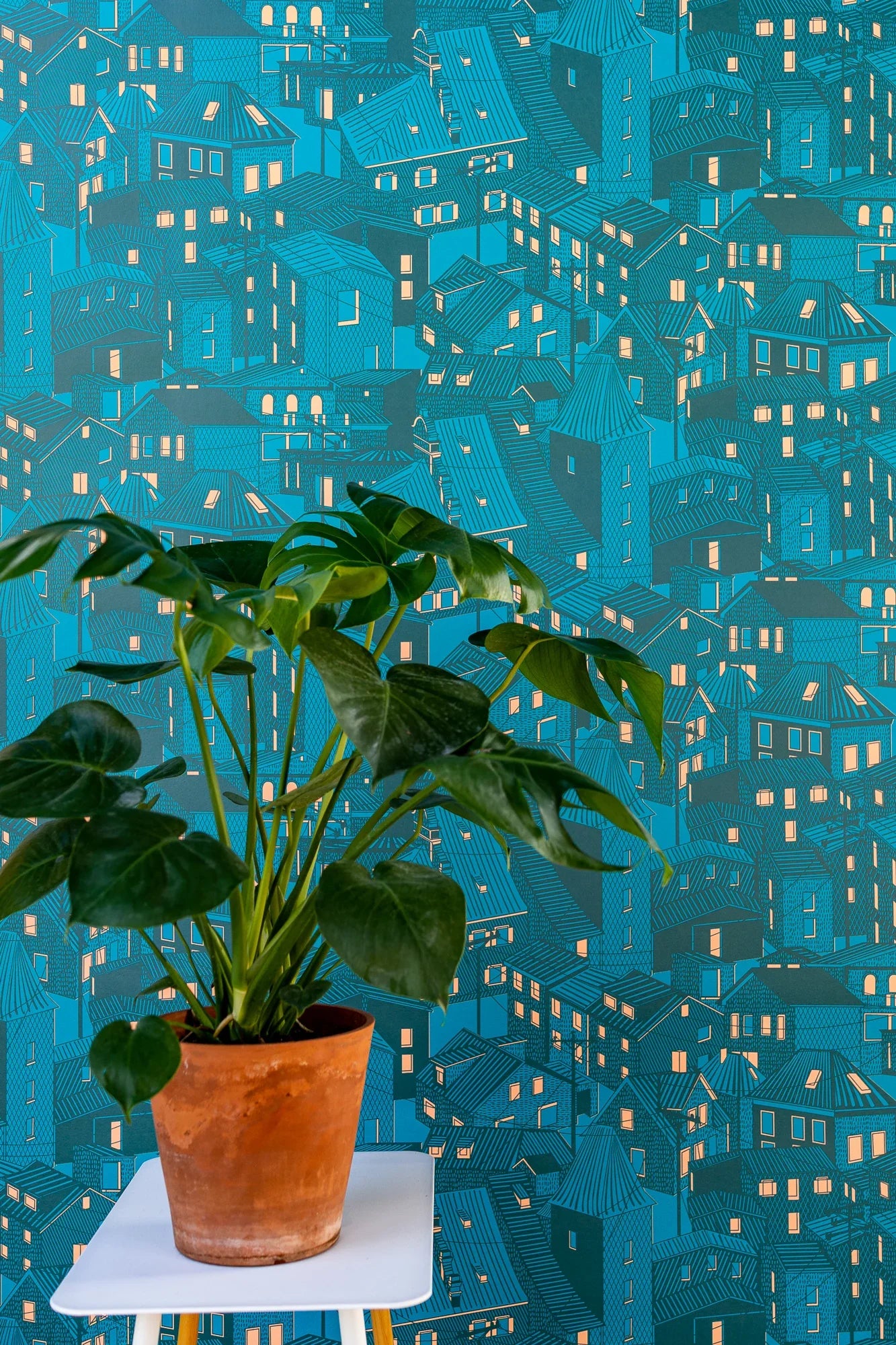 Monstera plant in terracotta pot on stool, blue cityscape wallpaper background