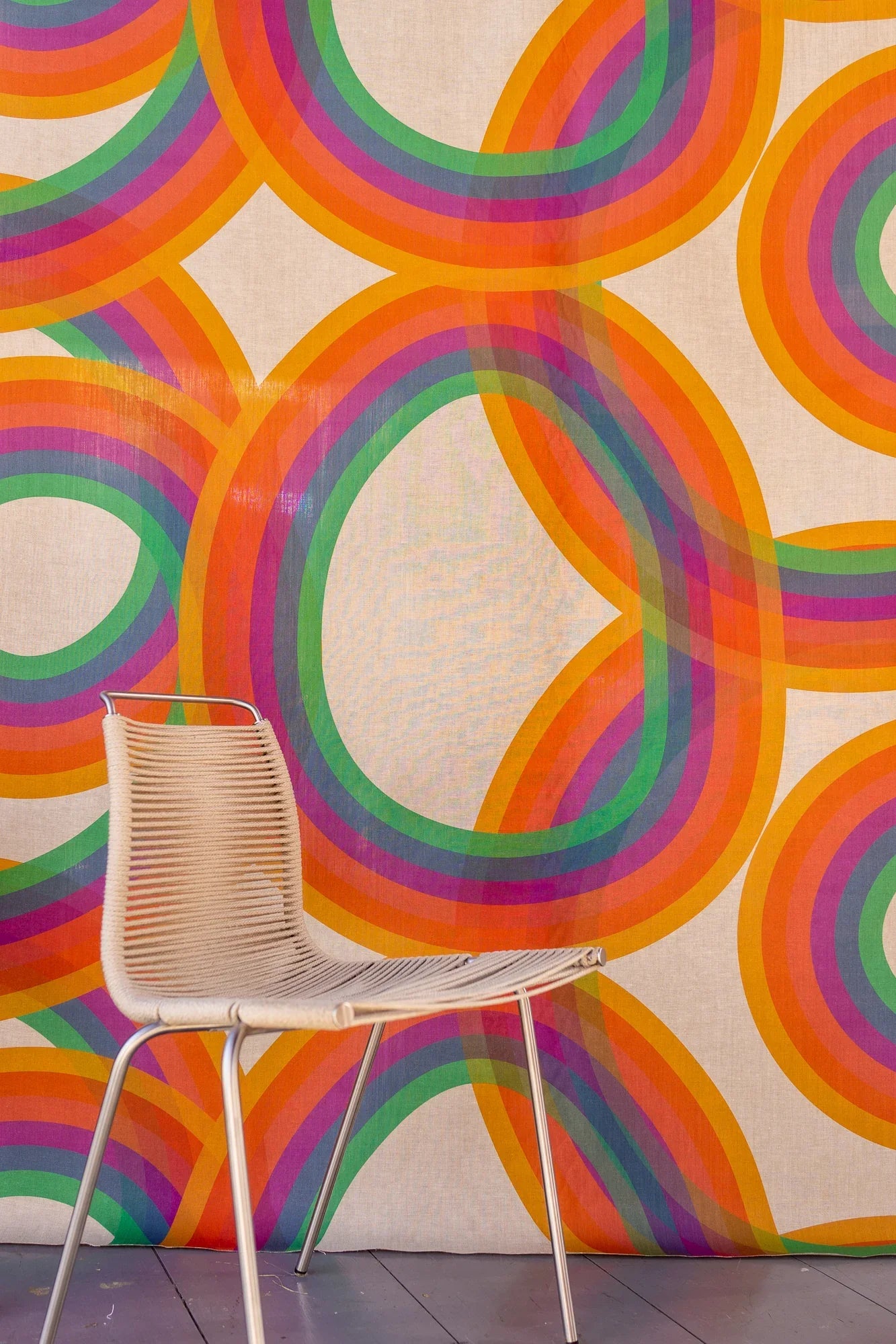 Modern rainbow linen wallpaper with bold overlapping arches and minimalist woven chair