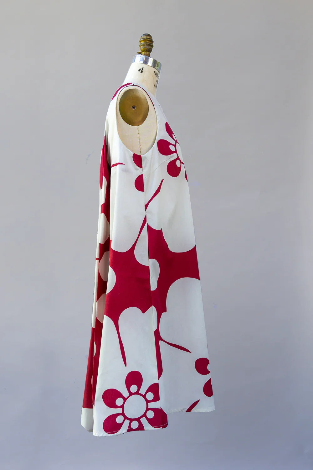 Sleeveless white muumuu dress with bold red Hawaiian floral print on a mannequin