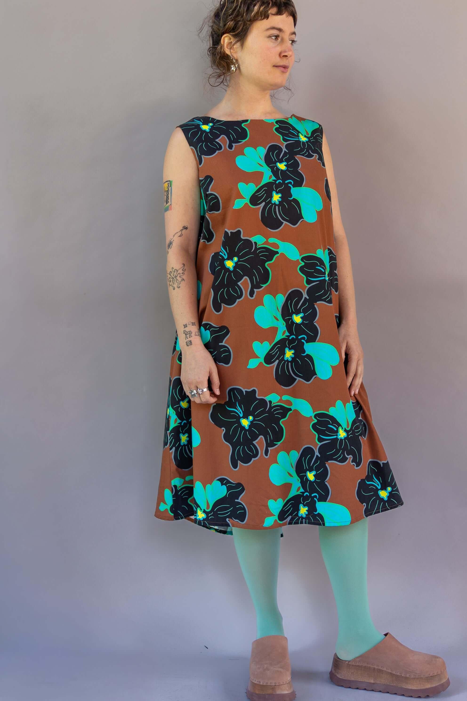 Woman wearing a sleeveless brown muumuu dress with bold teal and black Hawaiian floral print