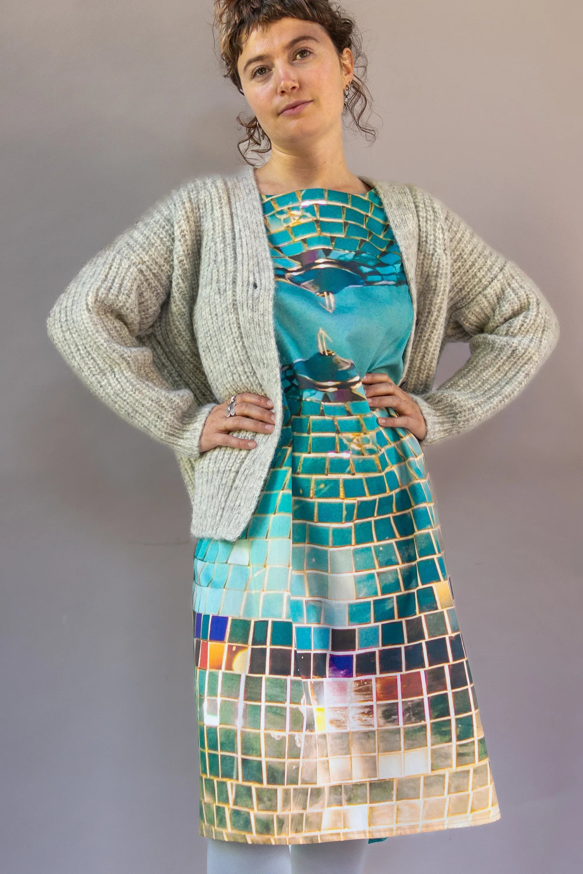 Woman wearing a modern printed dress with mosaic tile pattern and a chunky knit cardigan