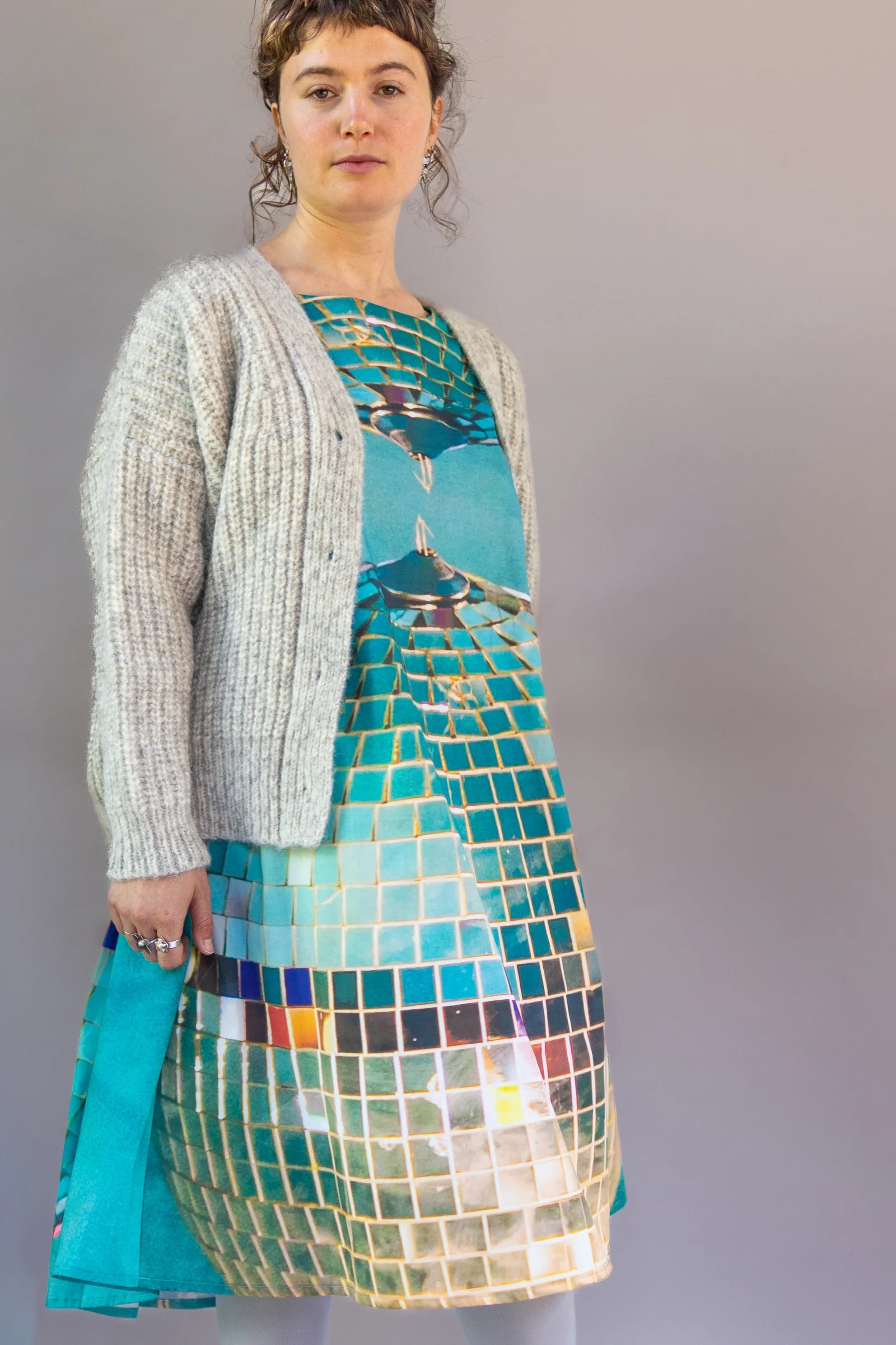 Woman wearing modern mu'umu'u dress with teal mosaic print and gray knit cardigan