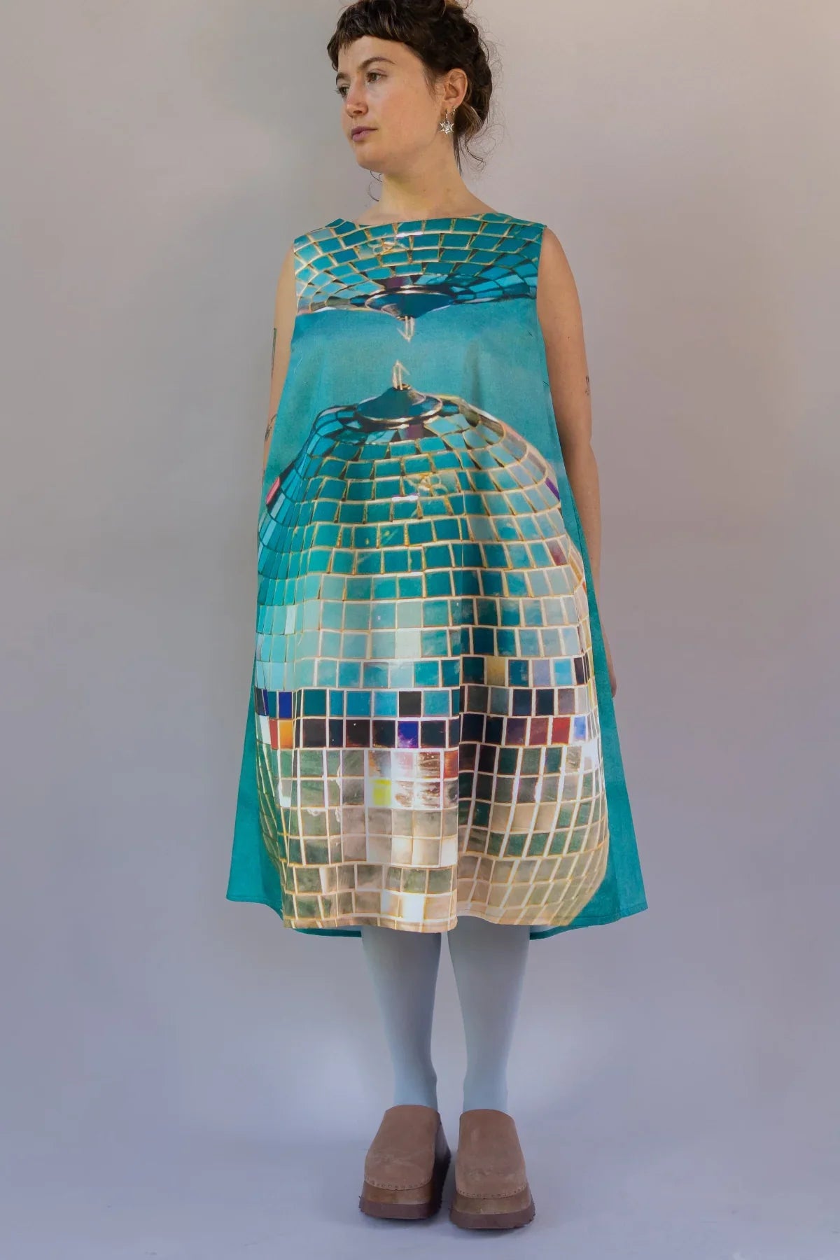 Woman wearing a teal modern mu'umu'u dress with disco ball print and neutral shoes