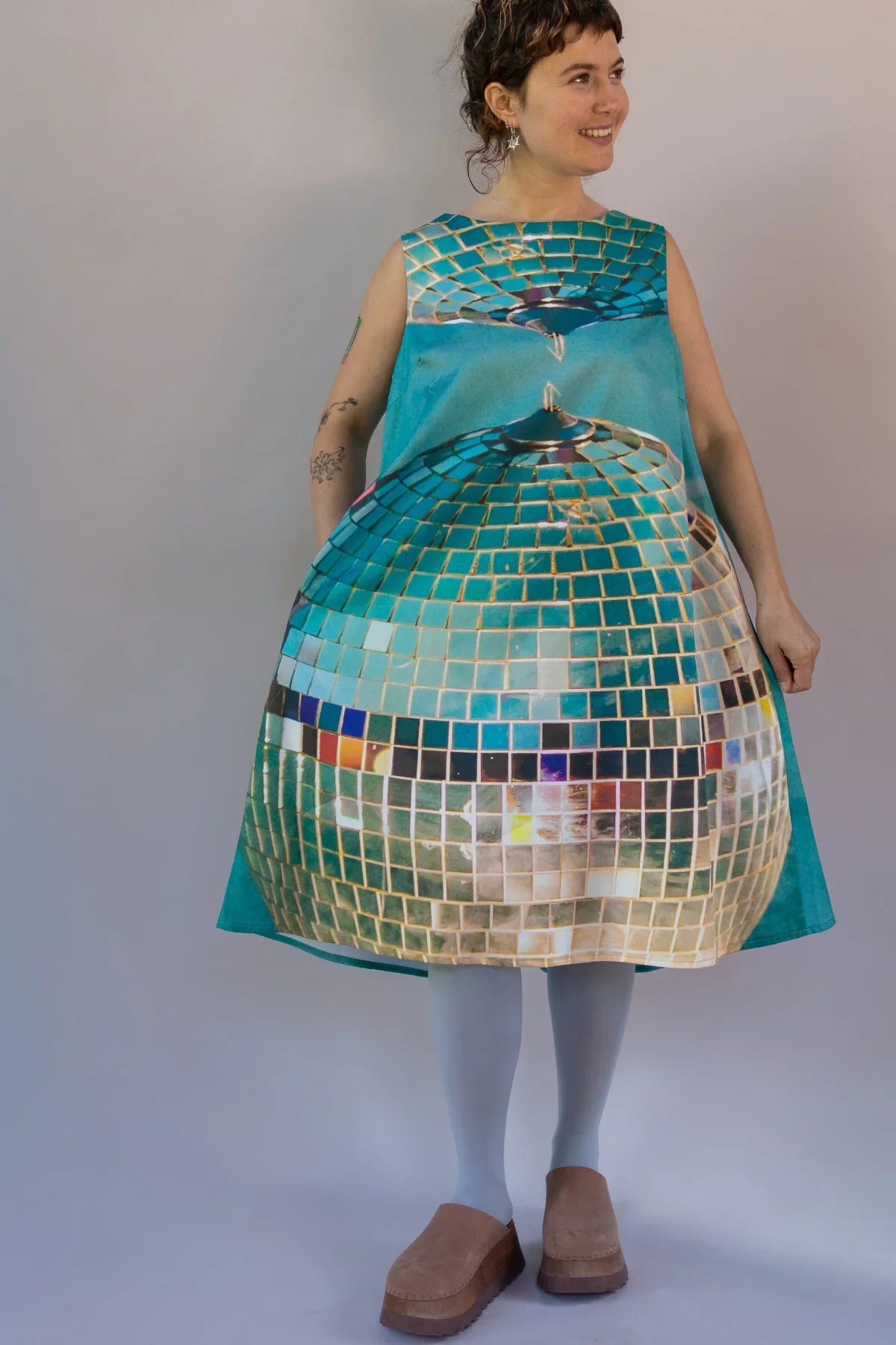 Woman wearing a sleeveless teal dress with a large disco ball print, modern muumuu style