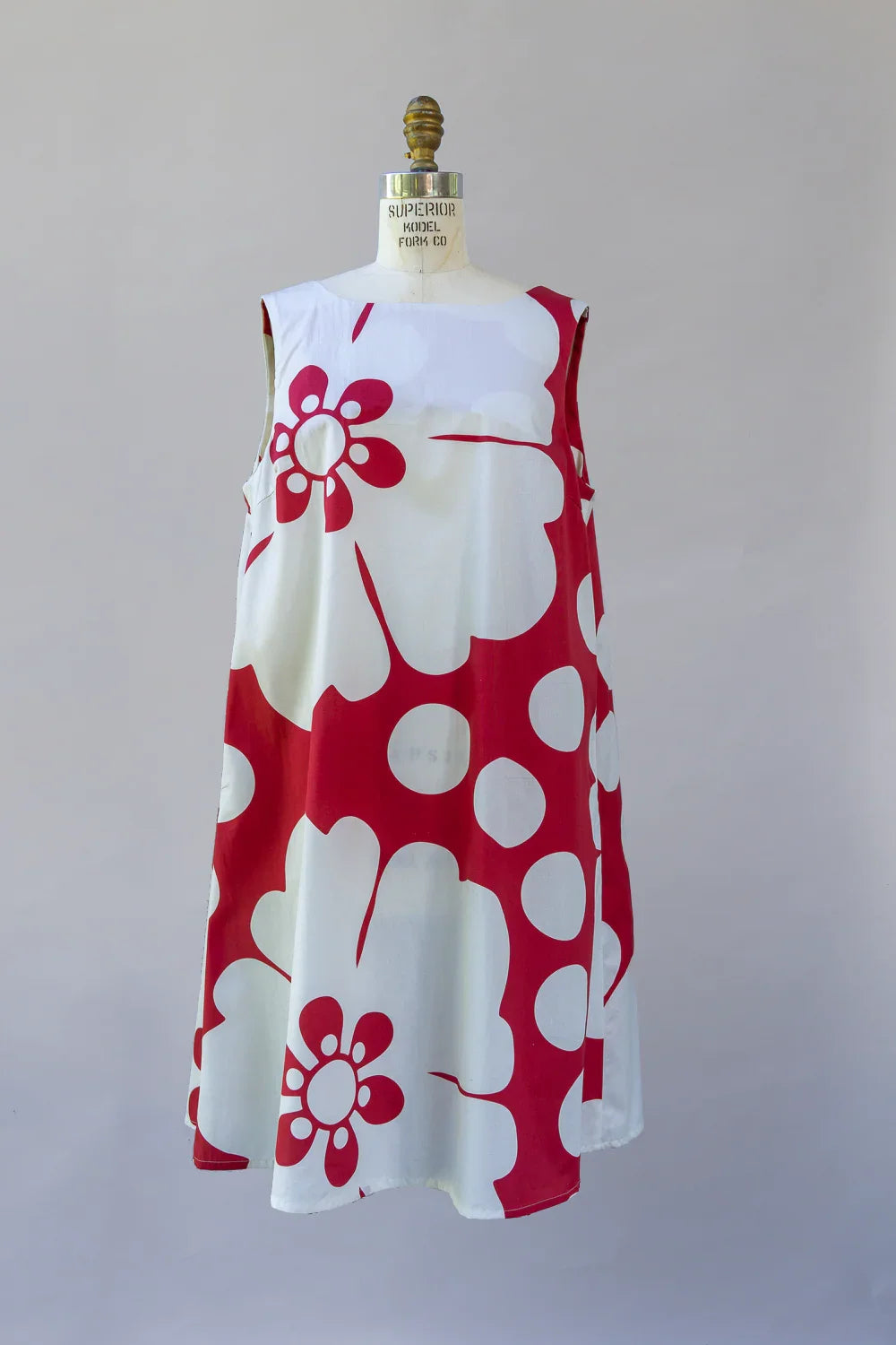 Sleeveless white muumuu dress with bold red Hawaiian floral print displayed on mannequin