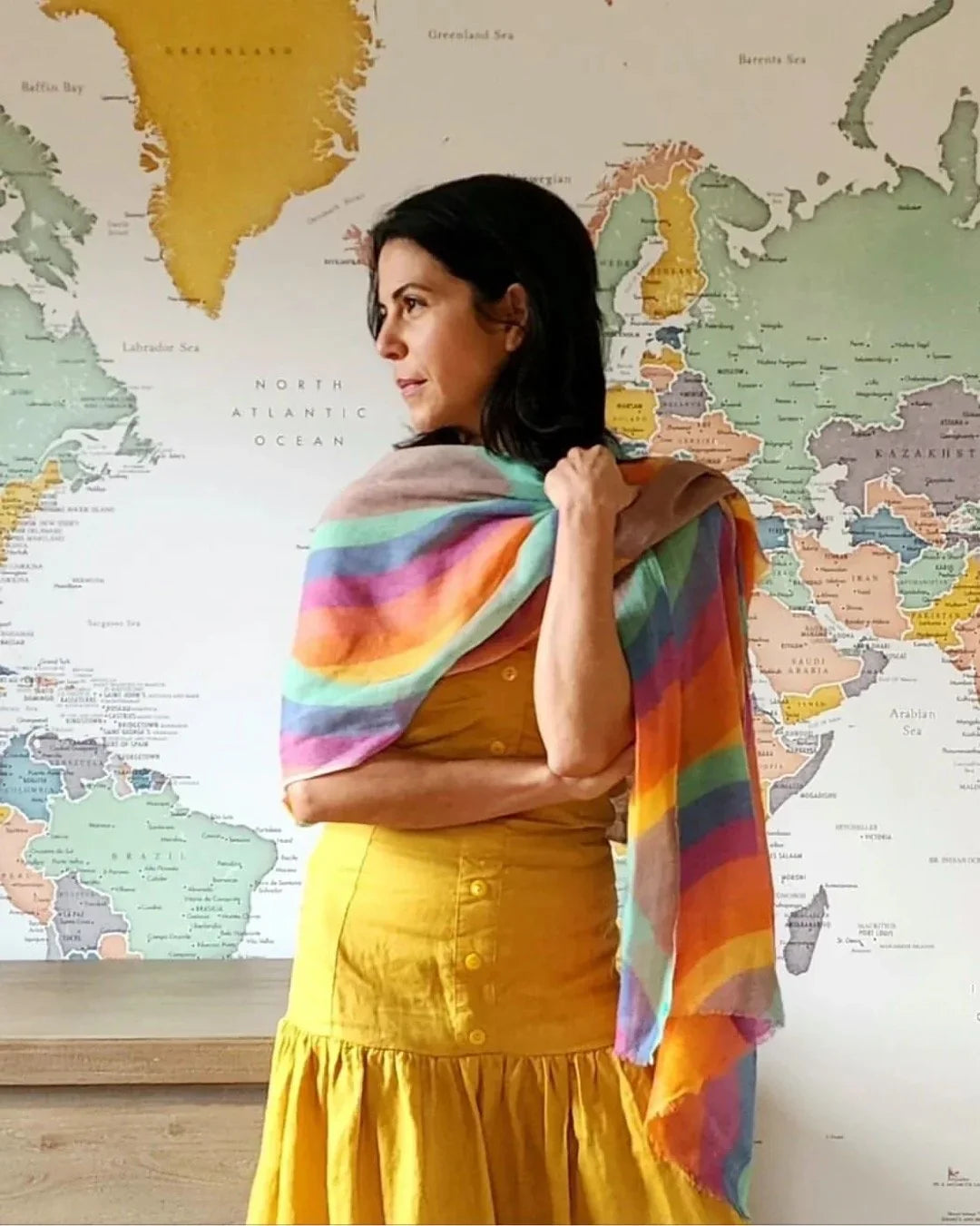 Woman in yellow dress with rainbow scarf standing in front of world map