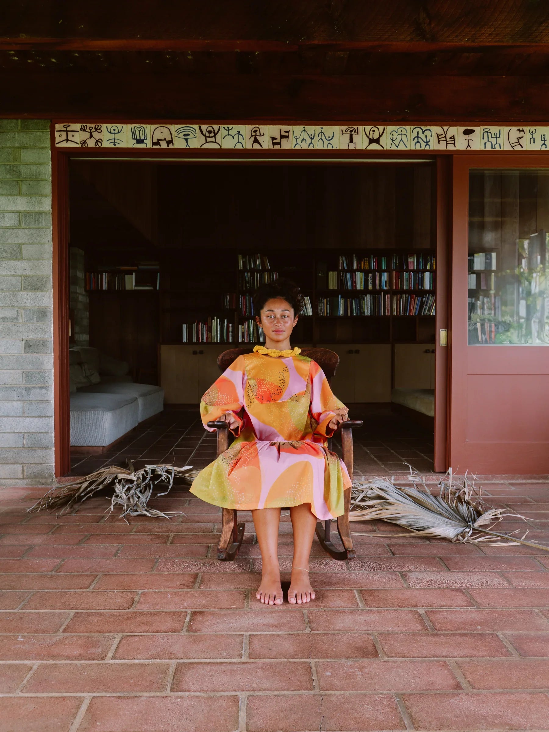 Woman in modern mu'umu'u dress with Hawaiian print sitting on a chair in a rustic setting