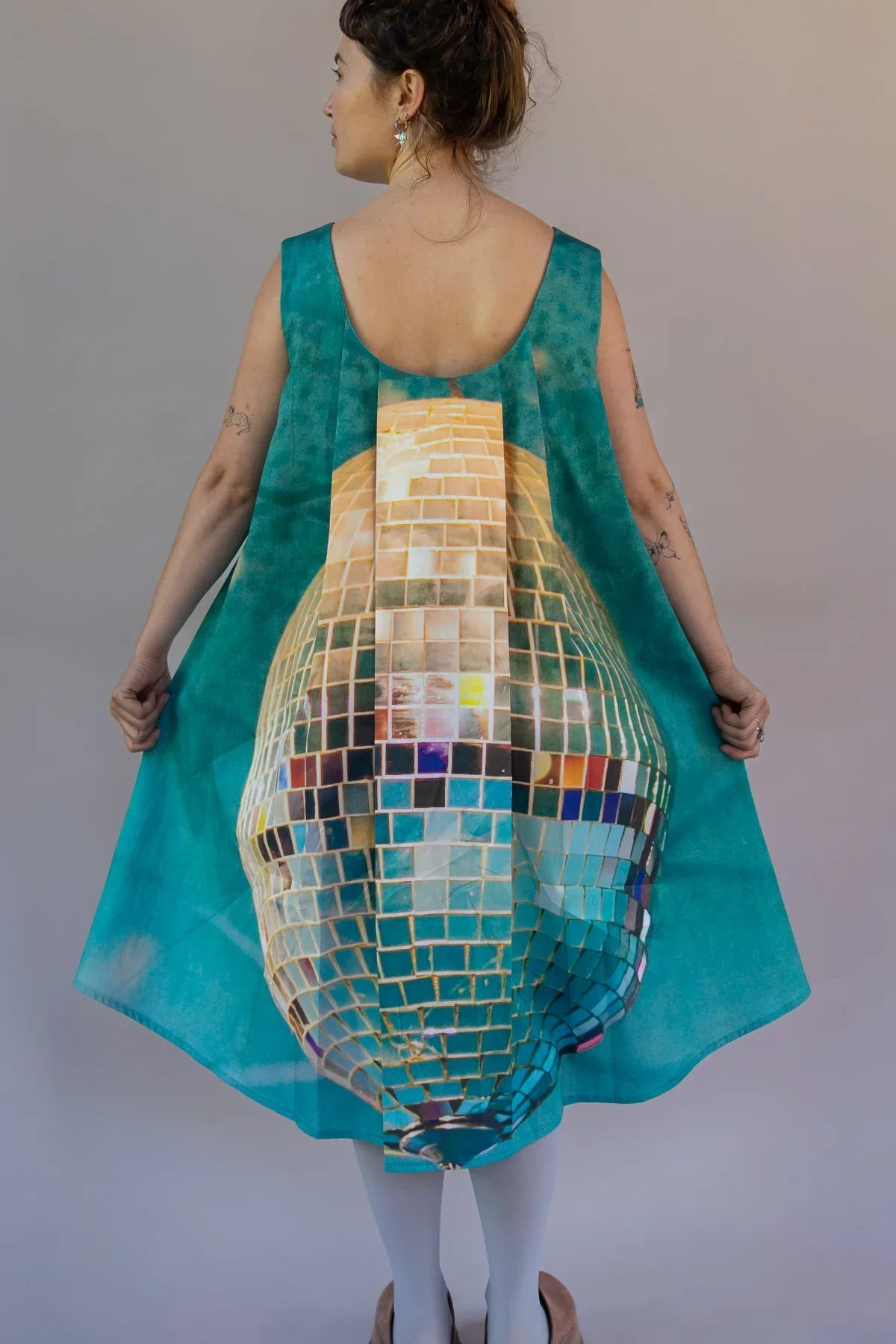 Woman wearing a sleeveless teal mu'umu'u dress with a disco ball print on the back
